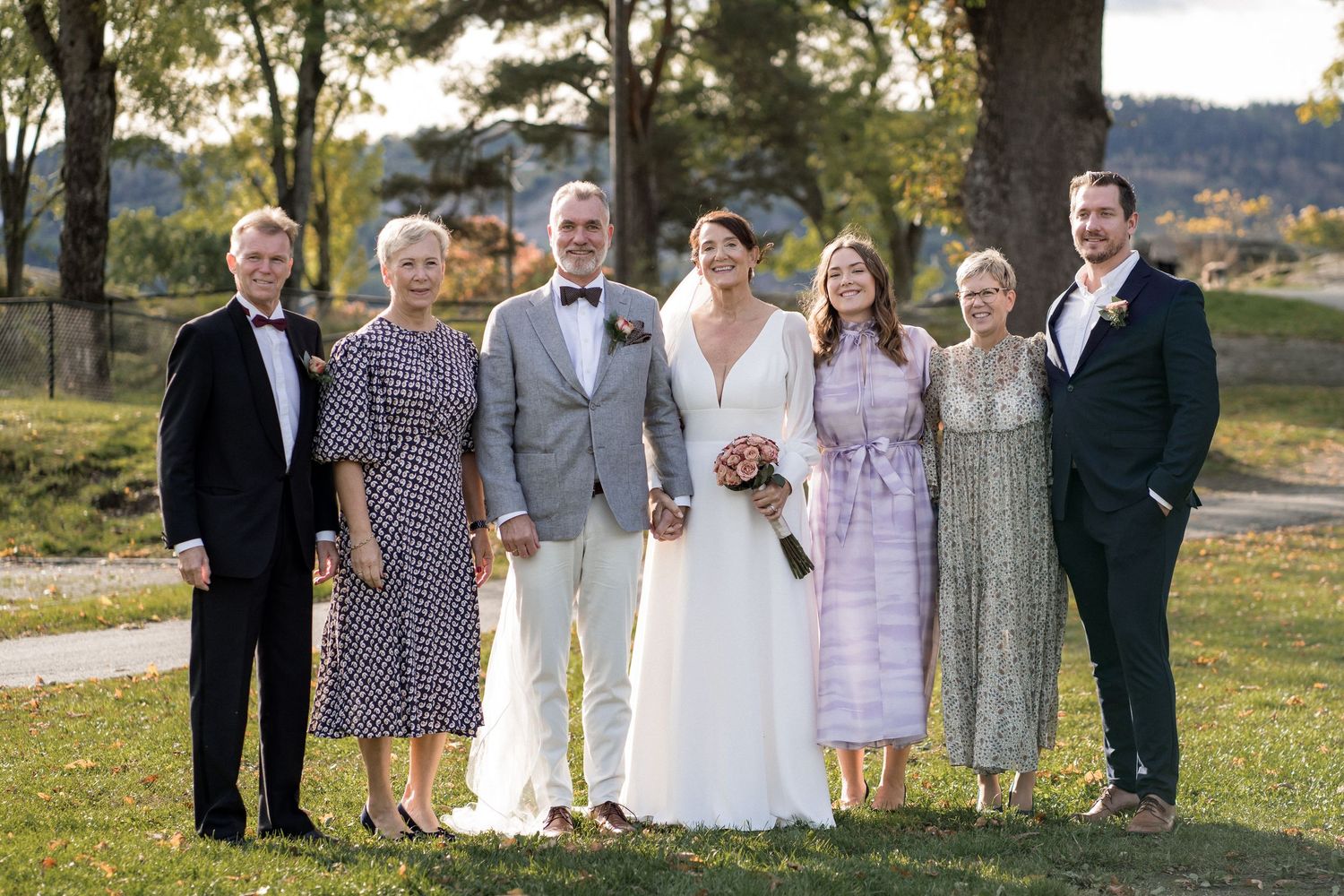 Wedding party posed outdoors under trees during golden hour.