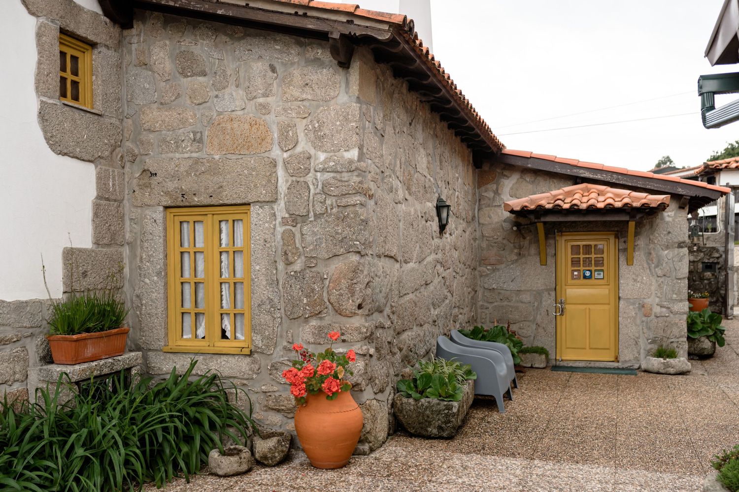 Stone cottage exterior with yellow doors and red flowers in rustic countryside setting.