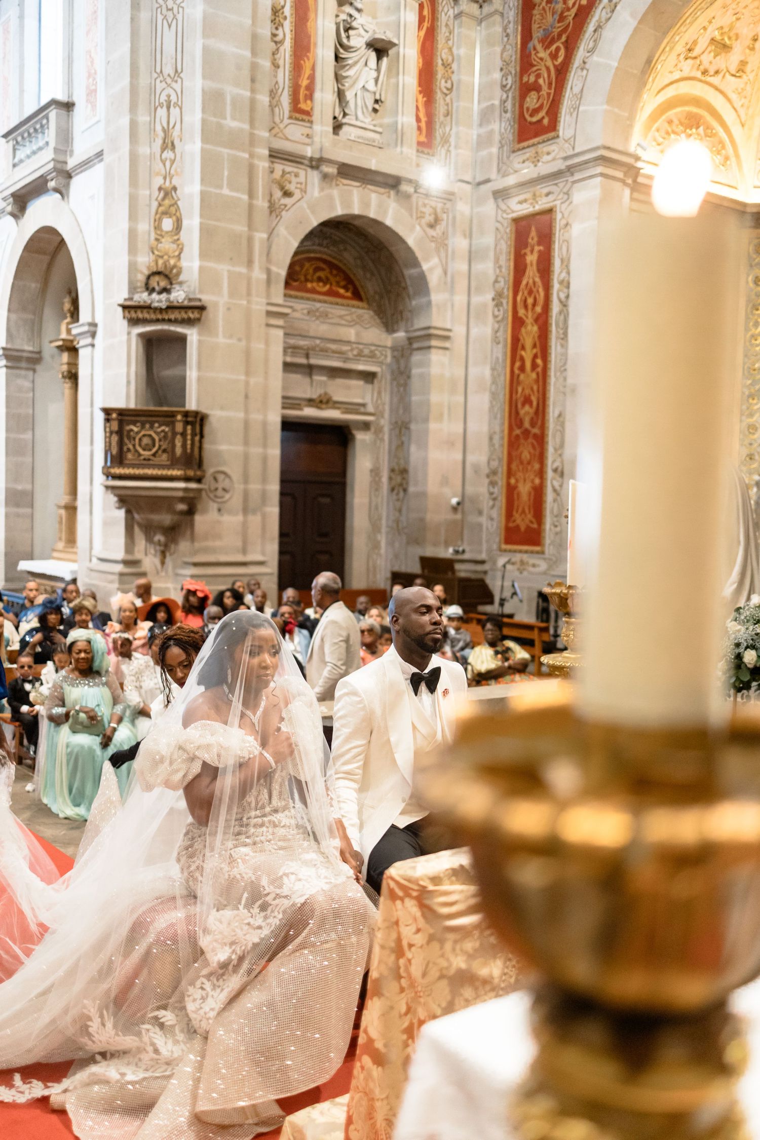 Ornate church interior filled with guests in white and pastel formal attire during a ceremony.