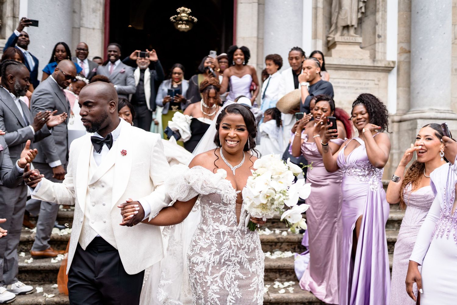 Wedding guests gather outside a grand venue entrance in formal attire.