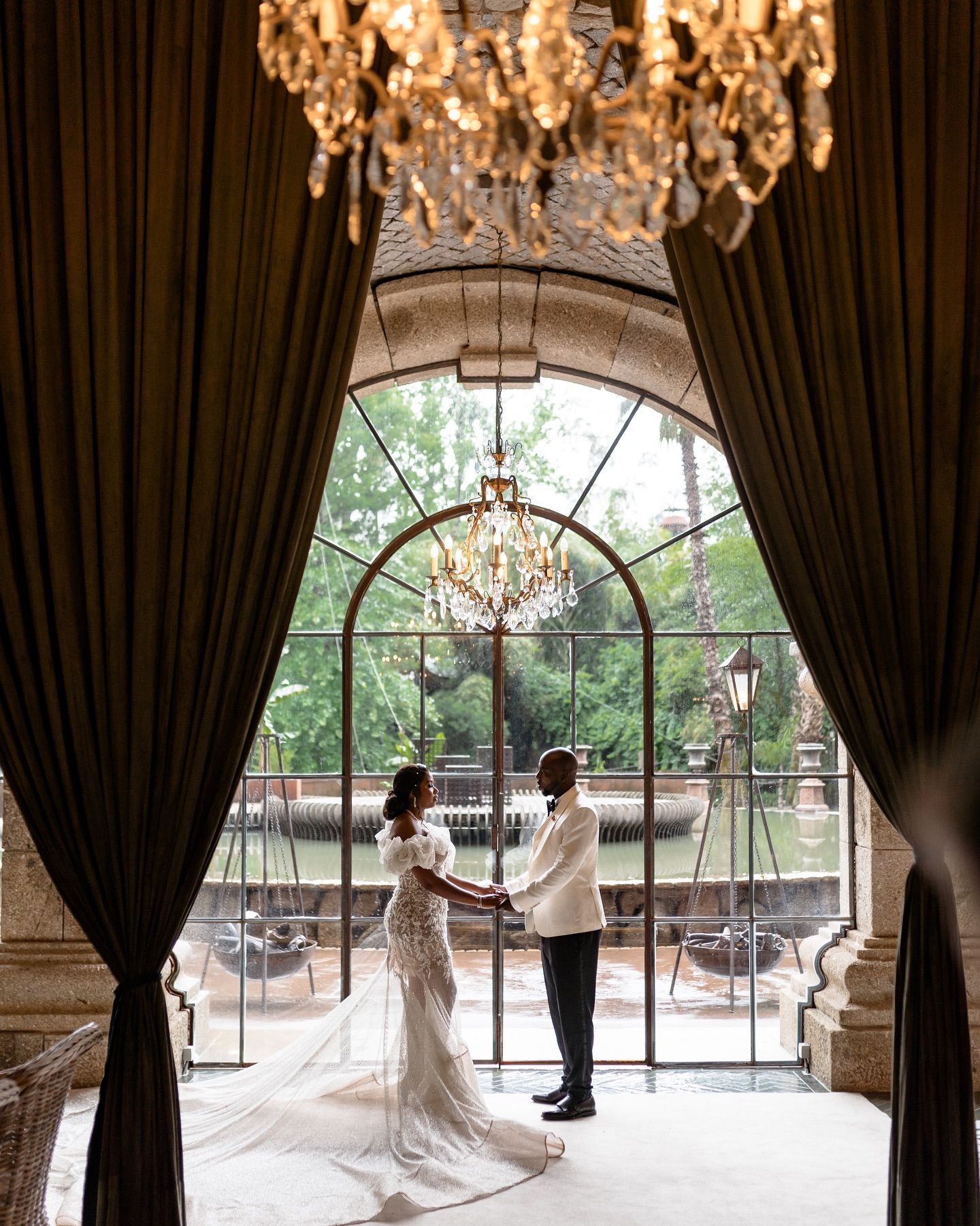 Wedding scene in elegant venue with crystal chandeliers and dramatic dark curtains.