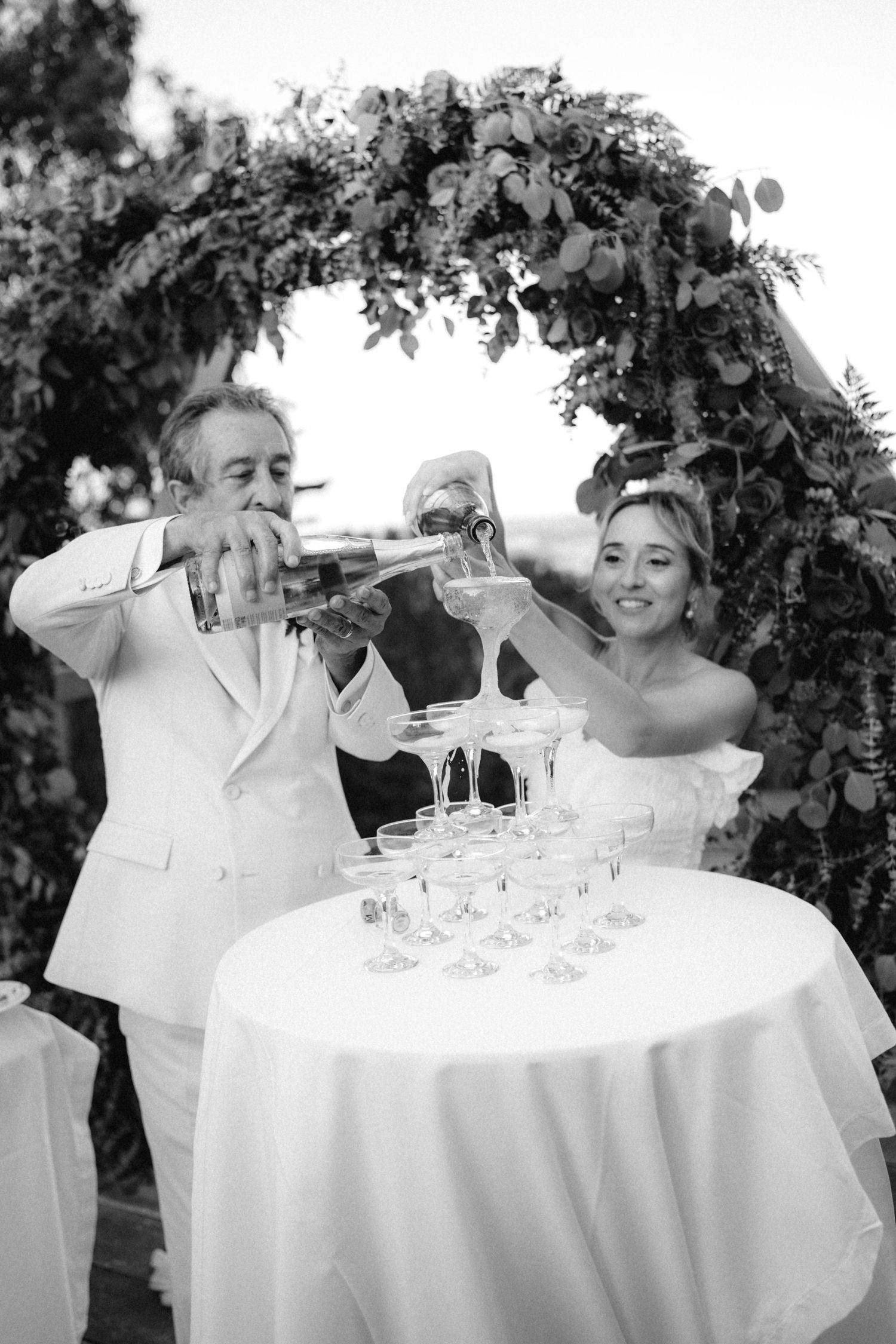 Black and white photo of champagne being poured into a tower of glasses at a wedding.