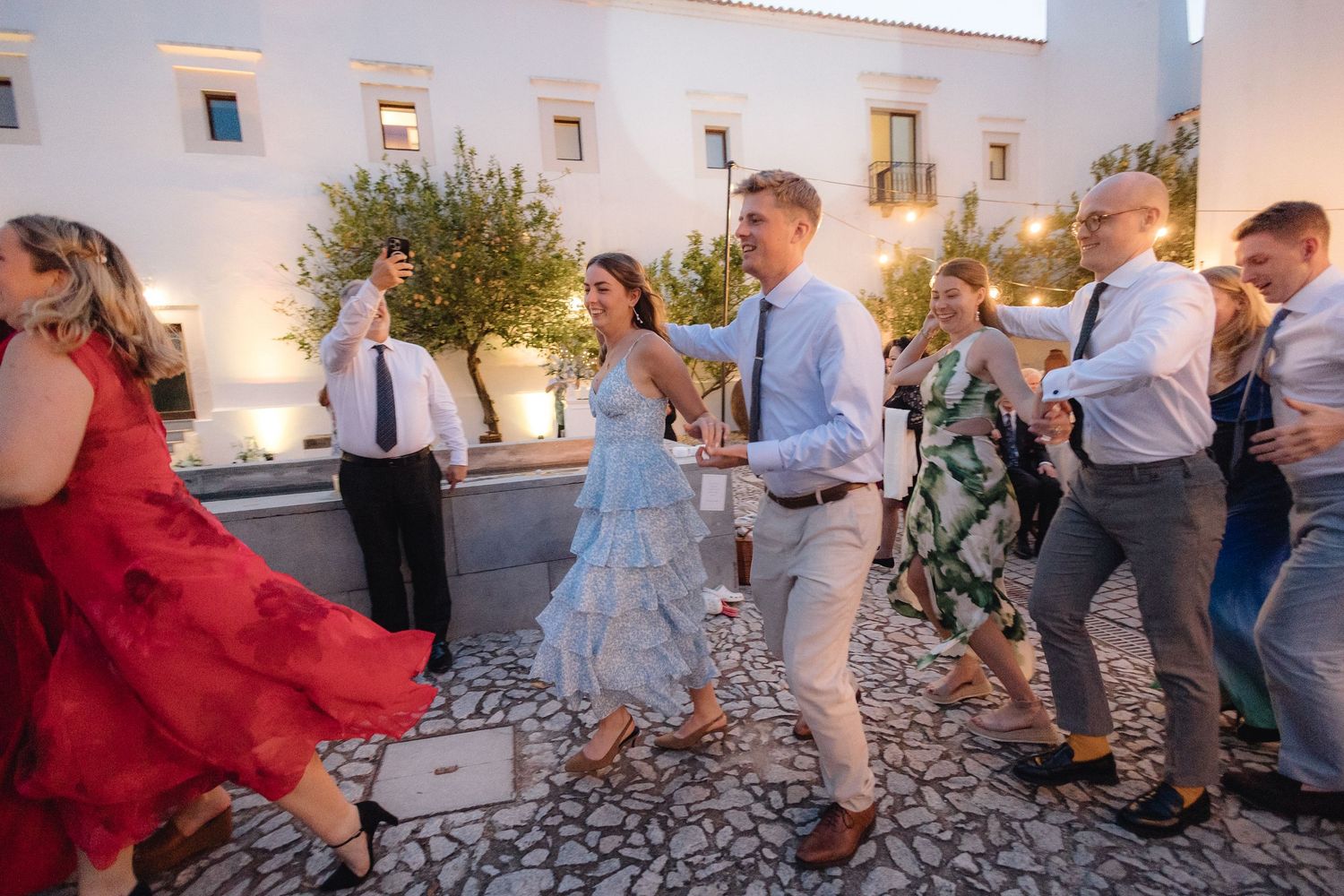 Wedding guests dancing and celebrating on stone patio during reception.