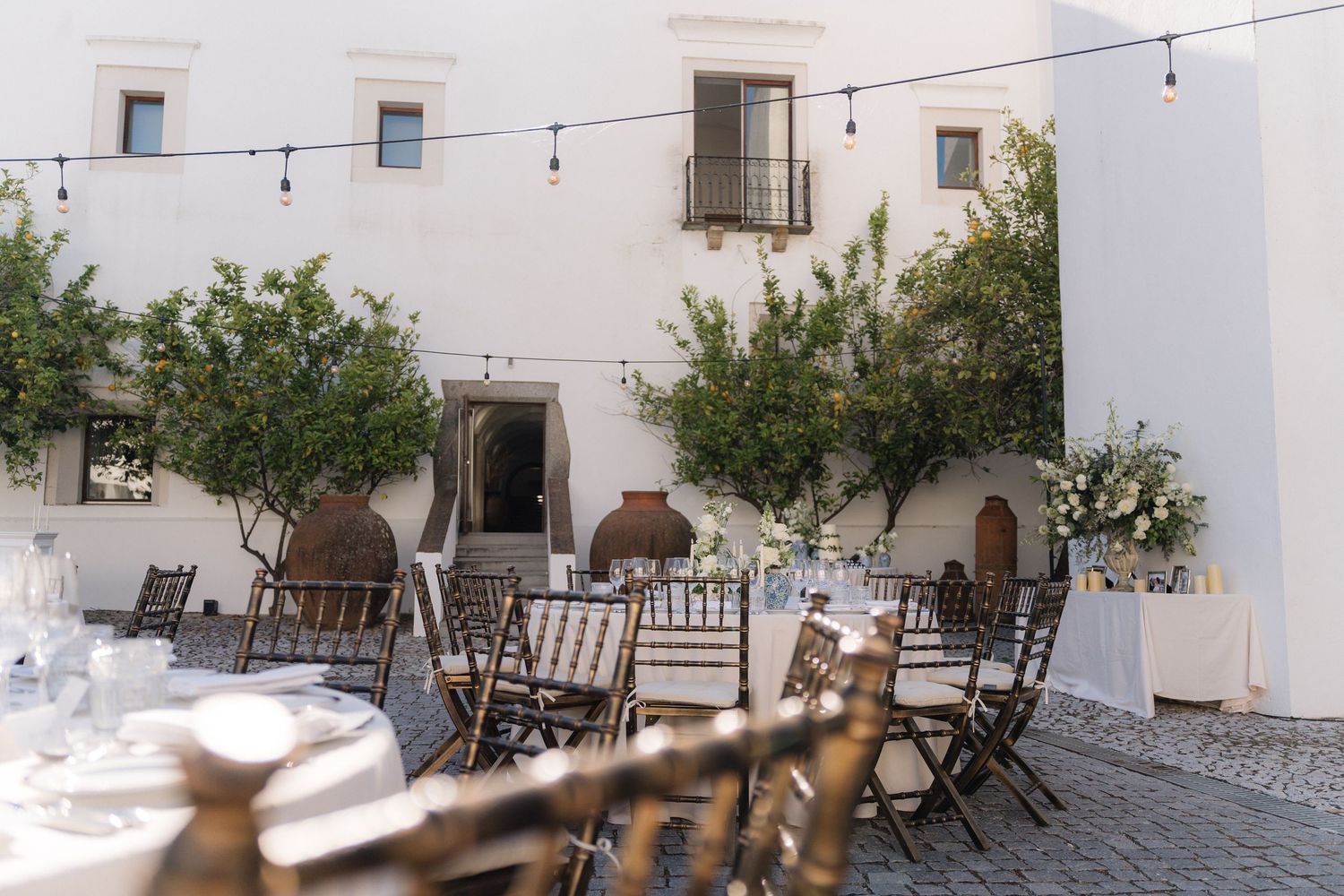 Mediterranean courtyard with string lights and white-washed walls set up for outdoor dining.