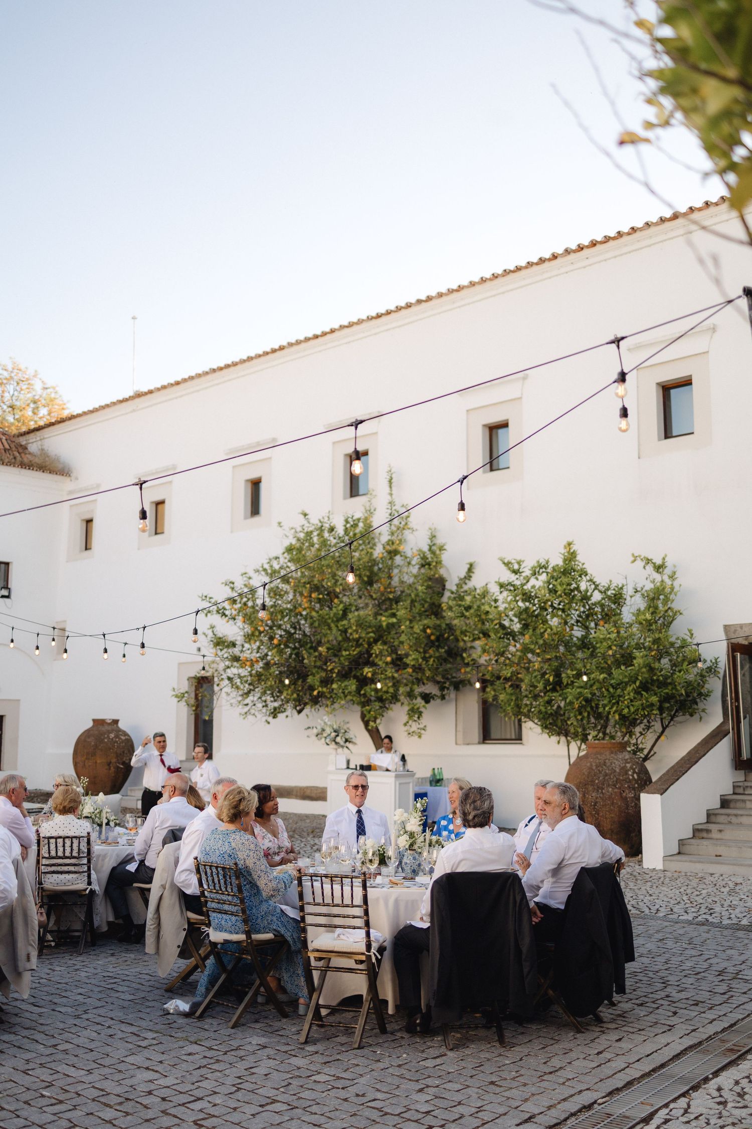 An outdoor wedding reception with string lights and white walls in a Mediterranean-style venue.