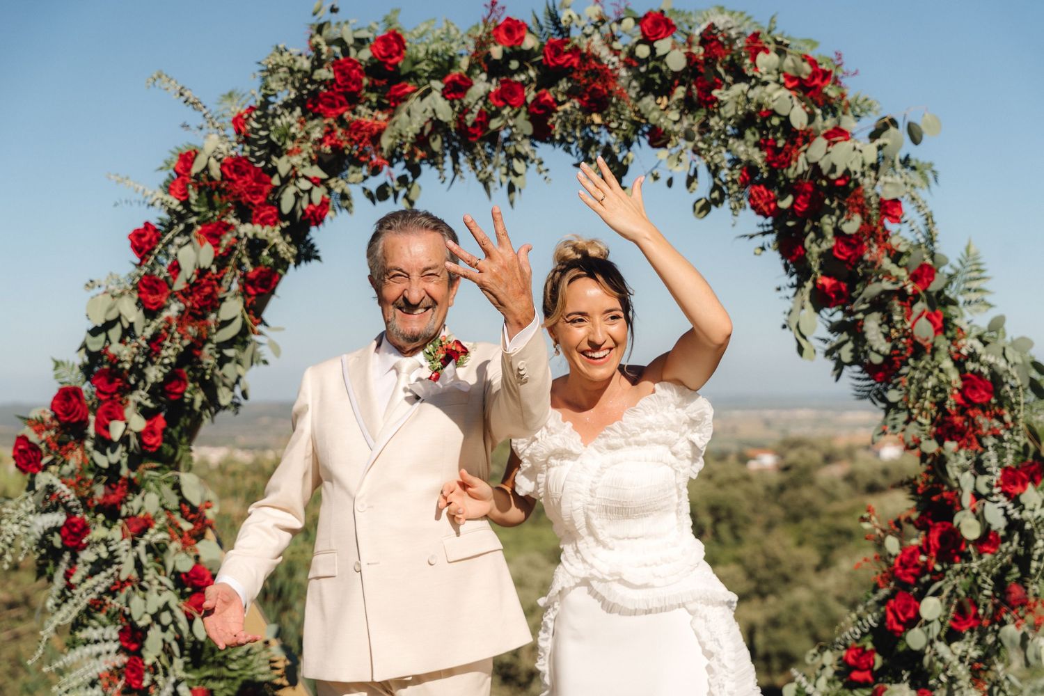 Beautiful floral arch with red roses decorates an outdoor wedding ceremony.