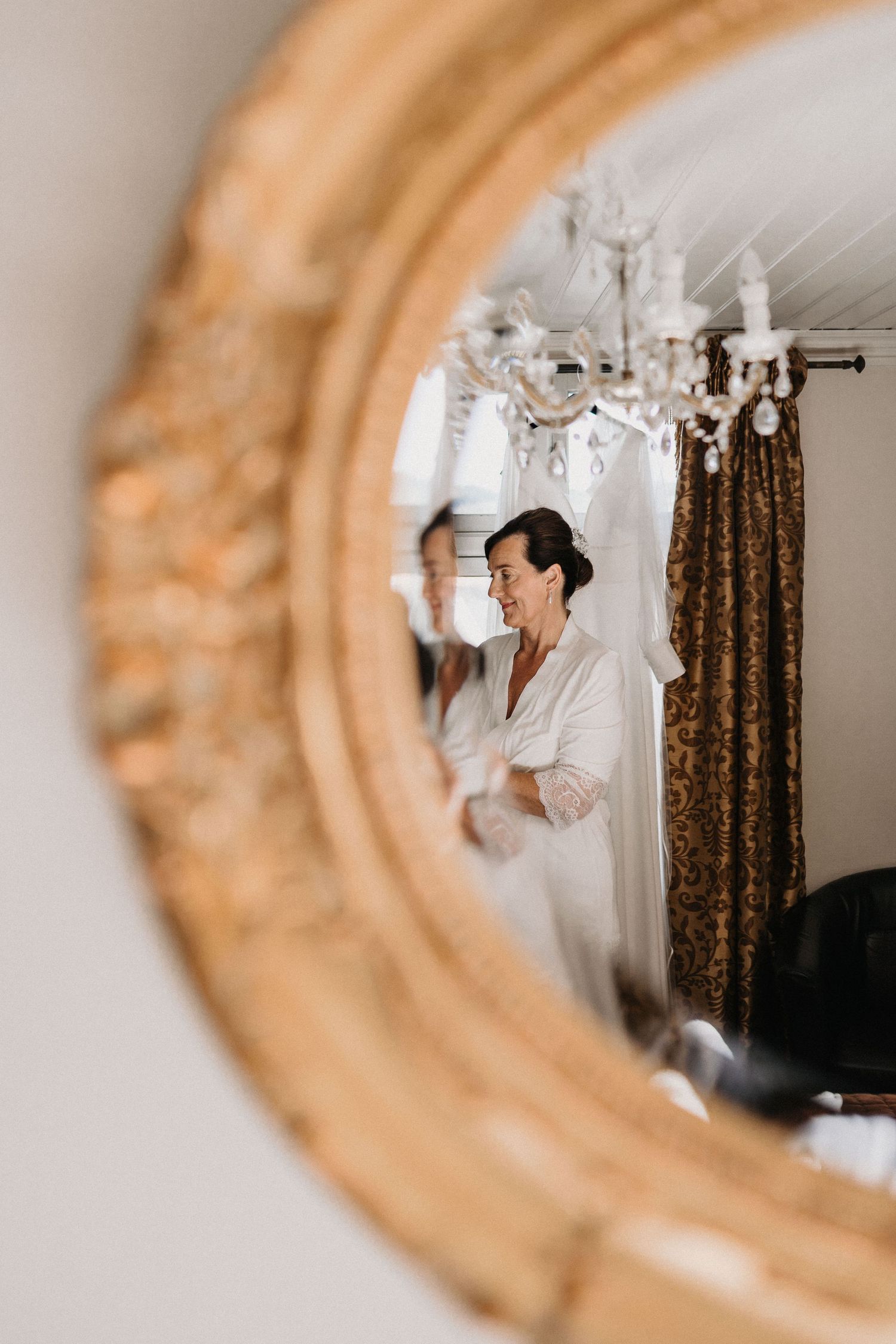 Reflection in an ornate gold mirror showing someone in white clothing.