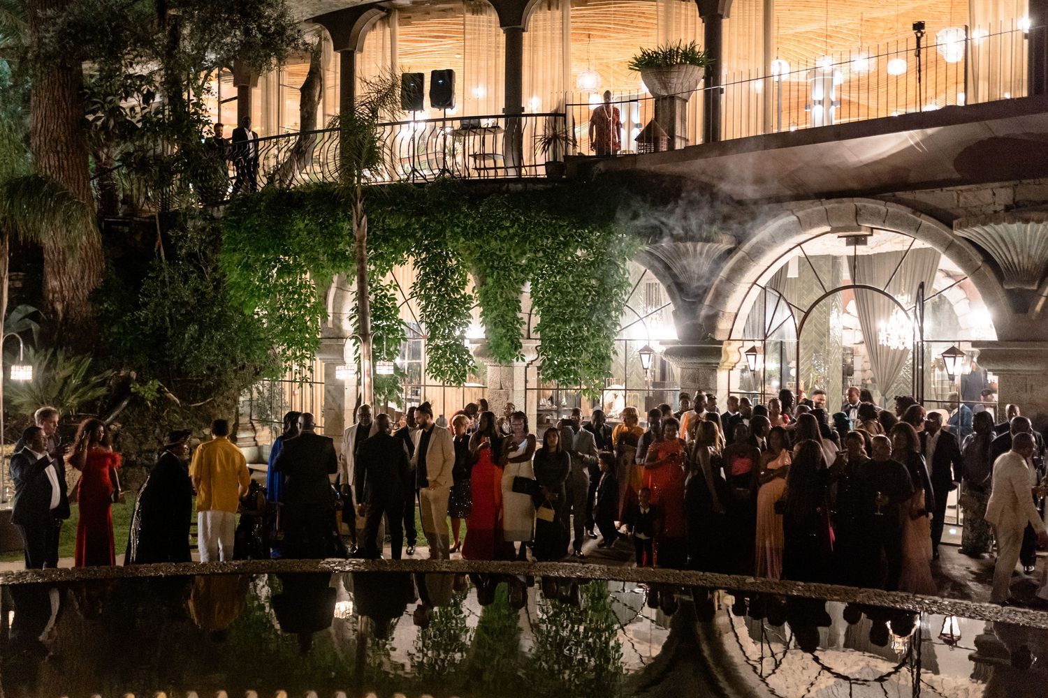 Large crowd of wedding guests gathered outside a beautifully lit historic building at night.
