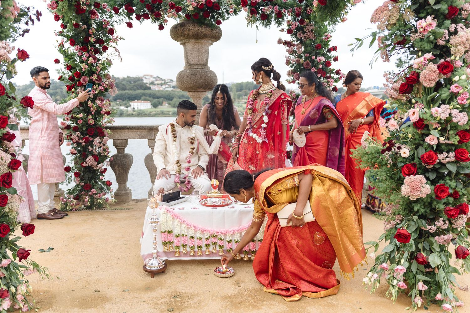 Beautiful floral arch with red roses decorates an outdoor wedding venue by the water.
