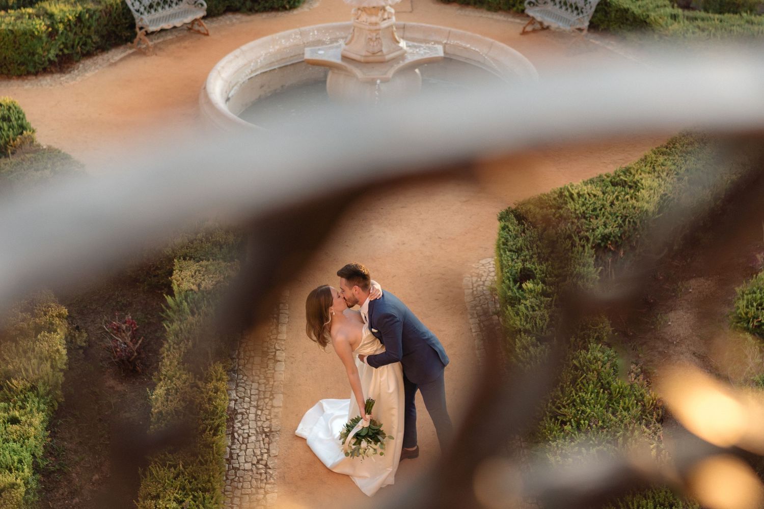 Overhead view of couple embracing near decorative fountain surrounded by manicured hedges.
