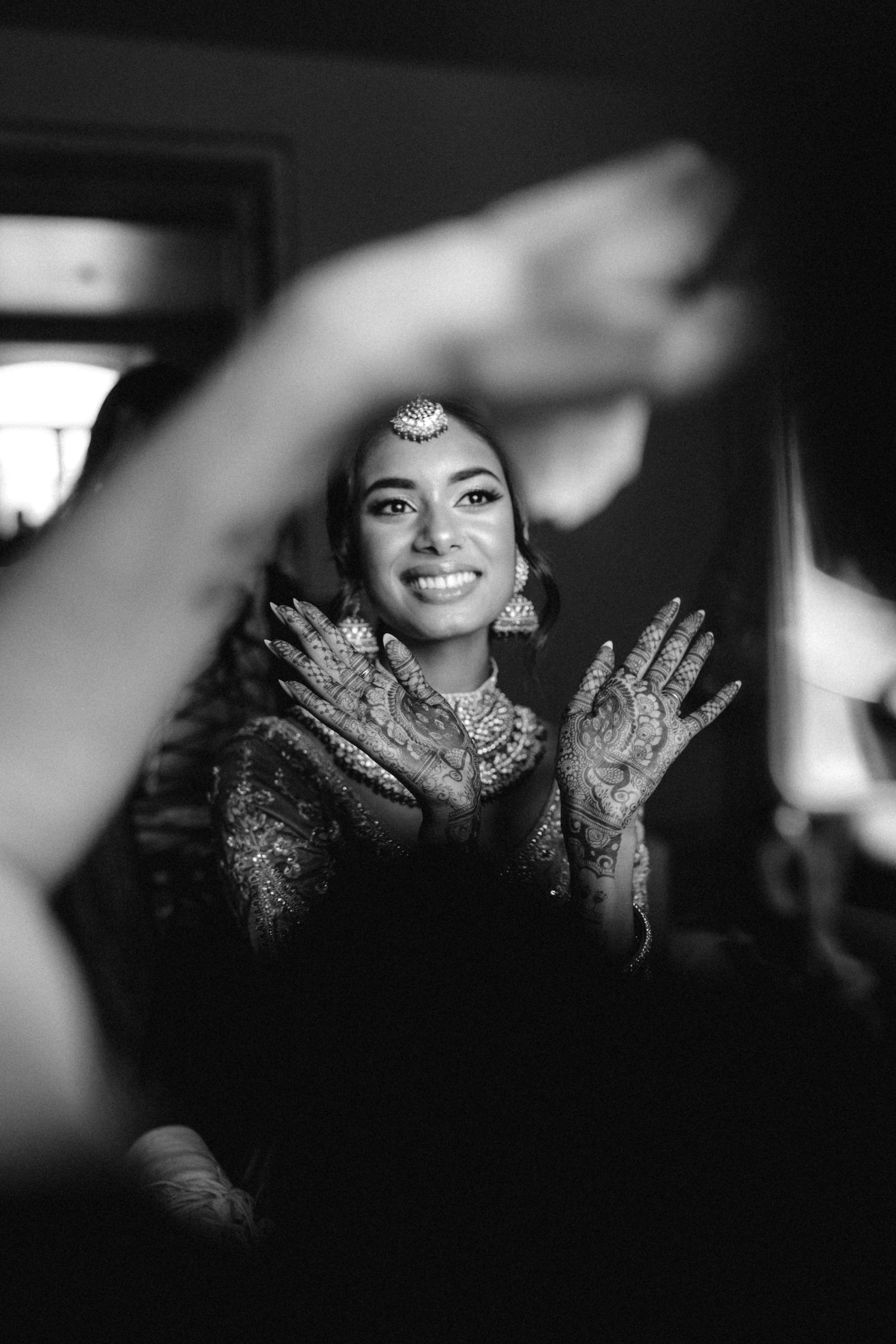Black and white portrait showing decorated henna hands and traditional bridal jewelry.