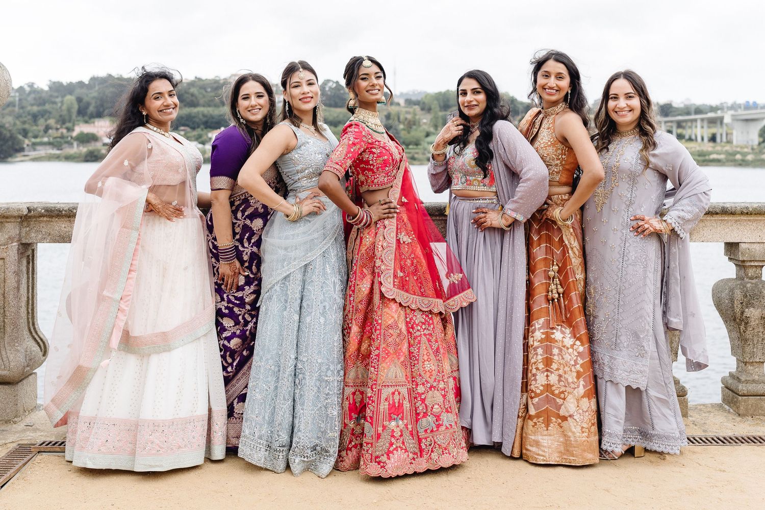 Wedding party members in pastel and floral dresses pose together by a waterfront setting.