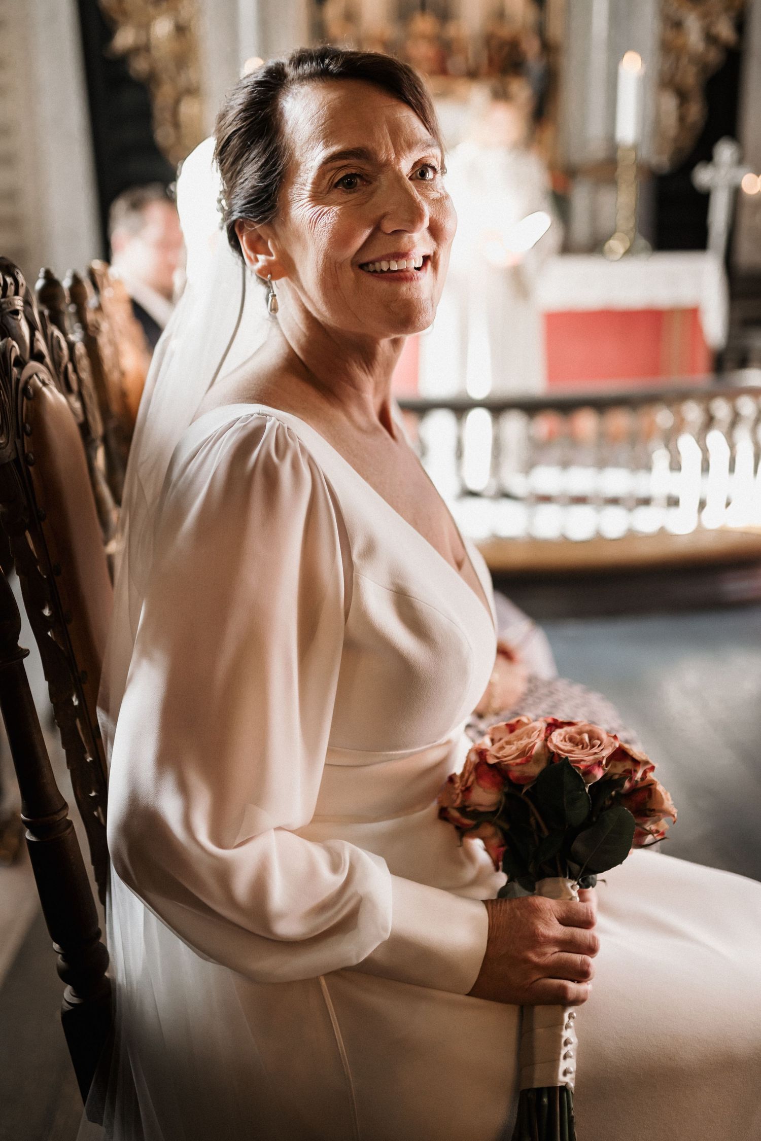 A radiant bride in an elegant white dress holding a bouquet of roses inside a church.