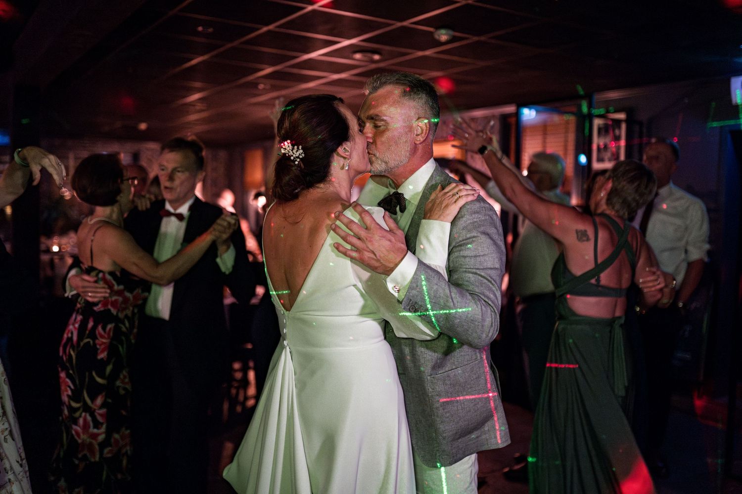 Wedding guests dancing under red mood lighting at an evening reception celebration.
