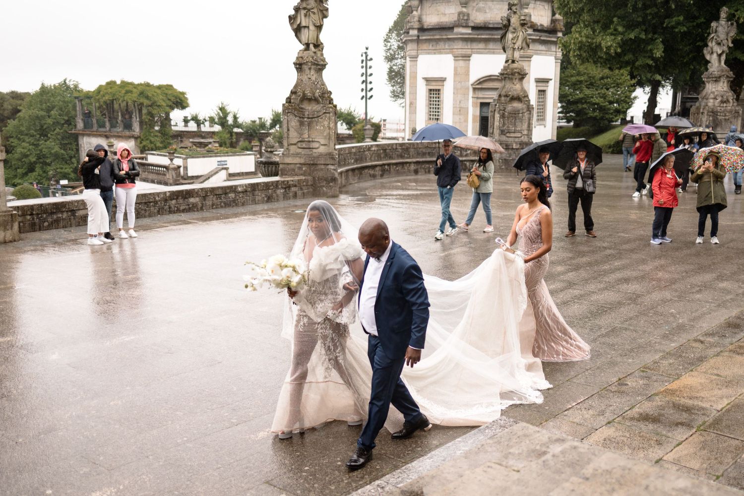 Wedding party walking on historic stone steps in light rain.