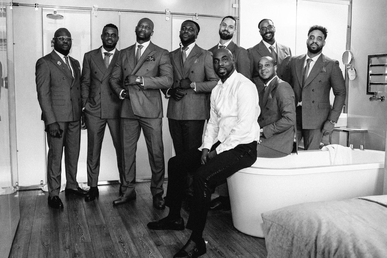 A group in formal attire stands together in a modern interior space with white walls and natural lighting.