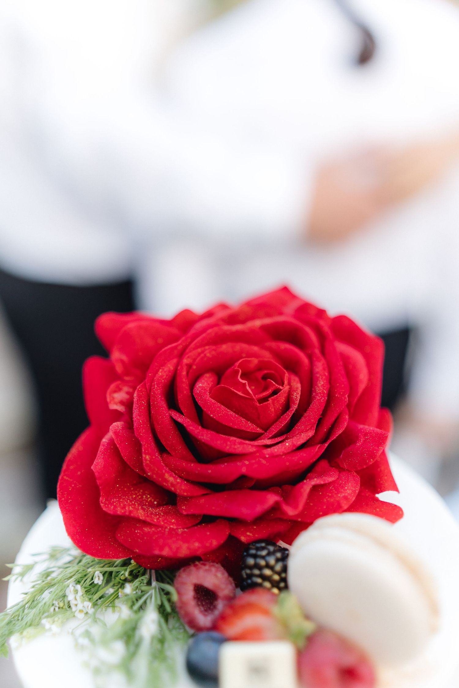 Detailed shot of a vibrant red rose adorning a white wedding cake with berries.