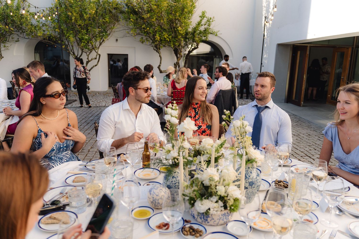 Guests enjoy an elegant outdoor dinner reception with floral centerpieces and string lights.