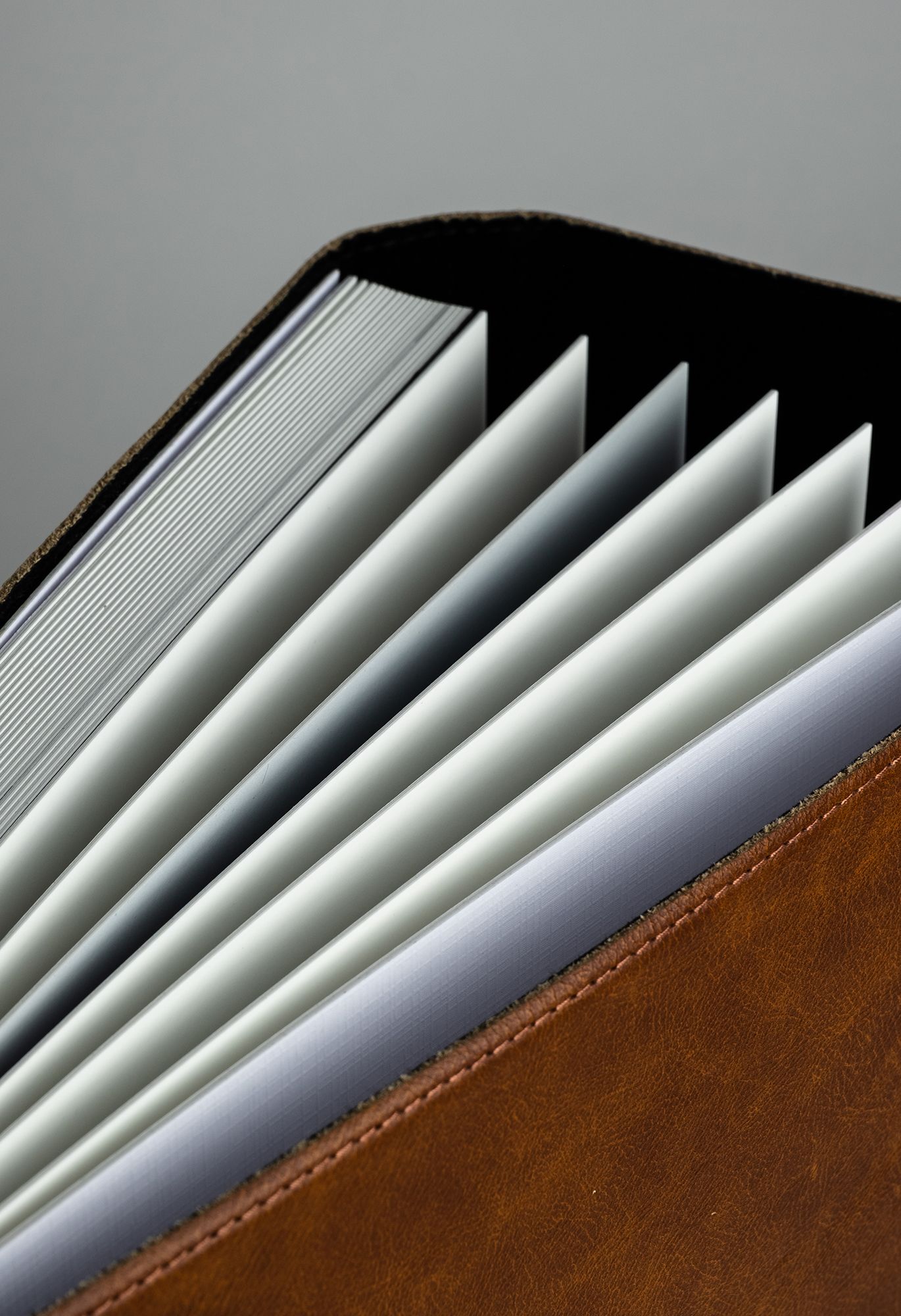 Close-up view of white paper pages fanning out against a brown leather surface showing crisp diagonal lines and shadows.