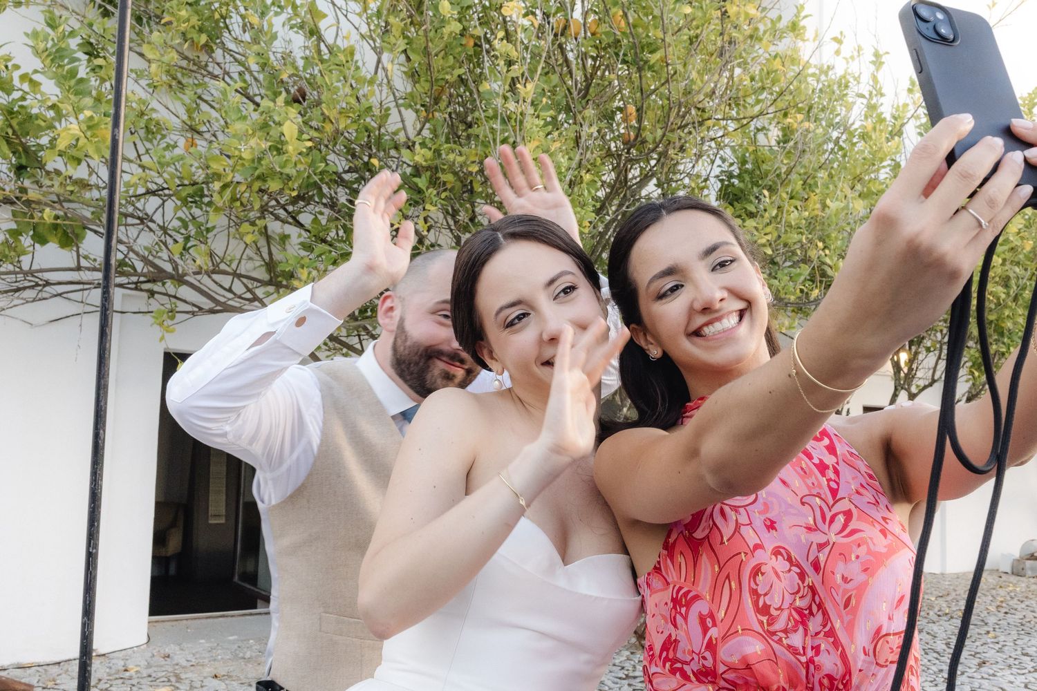 Wedding celebration with guests taking selfies and photos in a sunny courtyard.