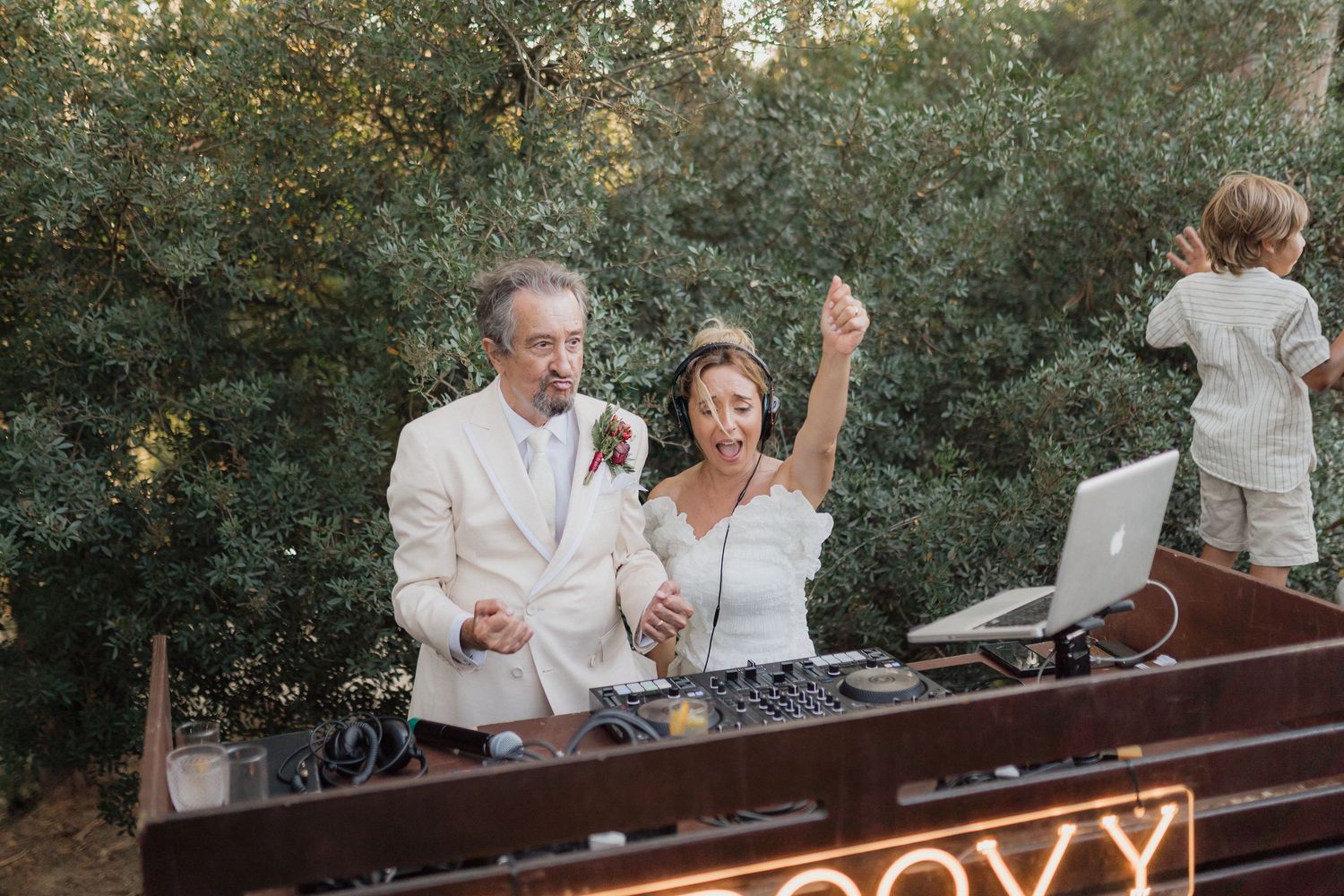 Wedding DJs working behind illuminated booth with 'Groovy' sign visible.