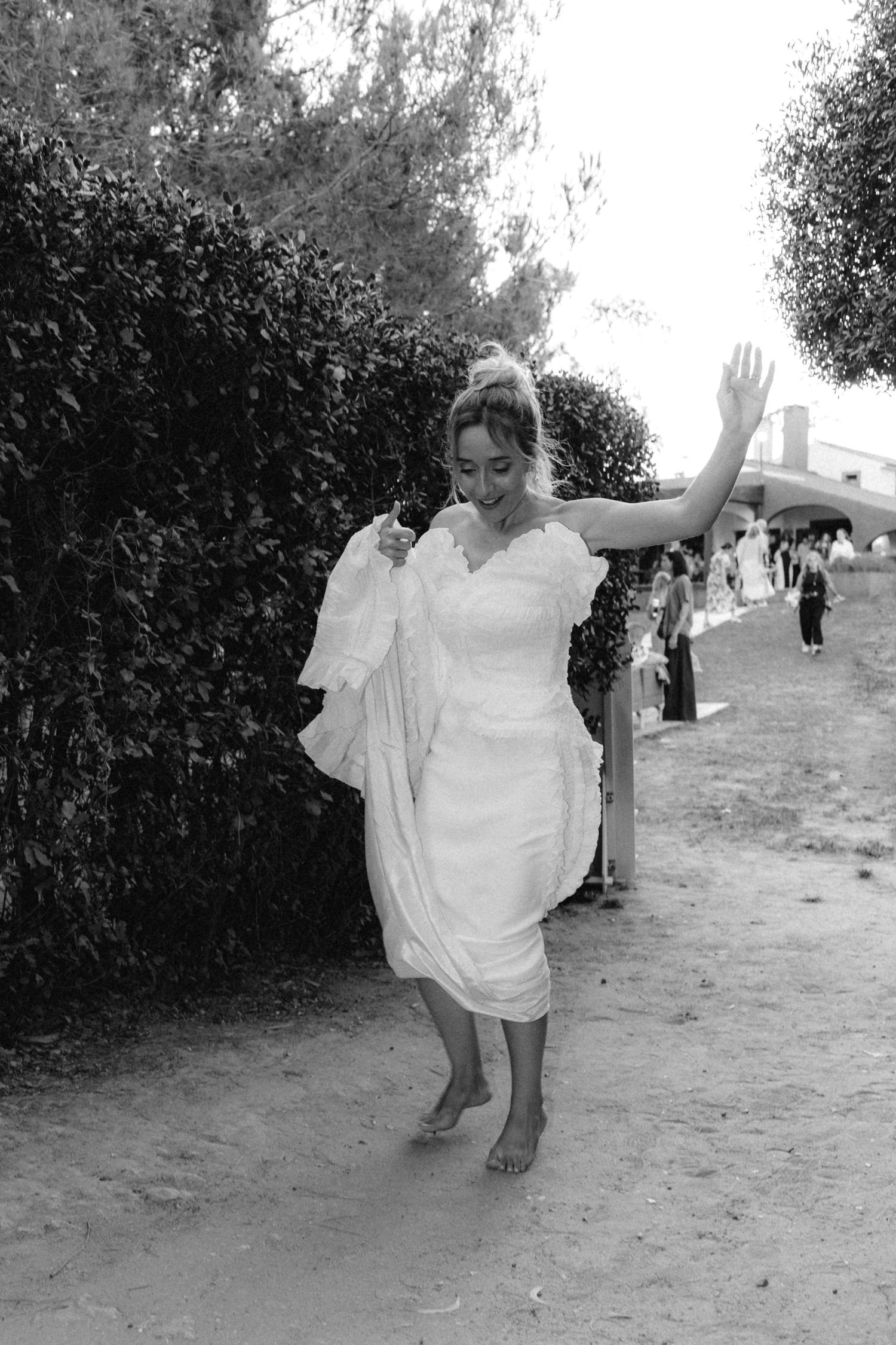 Couple in white attire dancing joyfully on outdoor path.