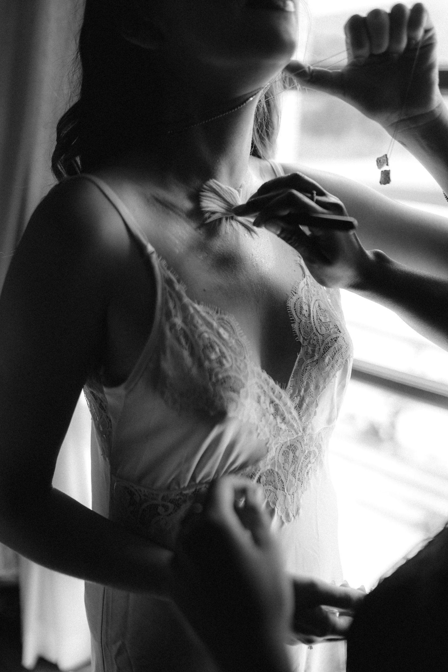 Black and white photo of a bride in lace wedding dress being helped to get dressed by bridesmaids.