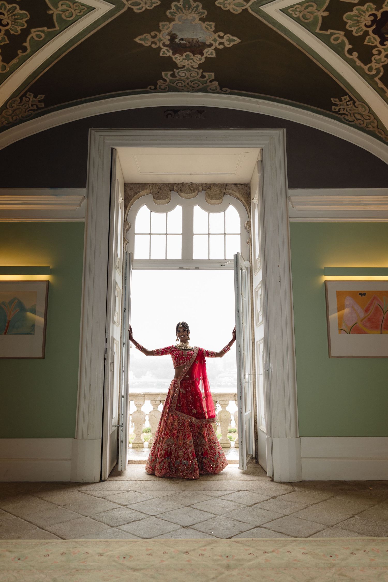 A dramatic silhouette of a red dress against large arched windows in an ornate room with green walls.