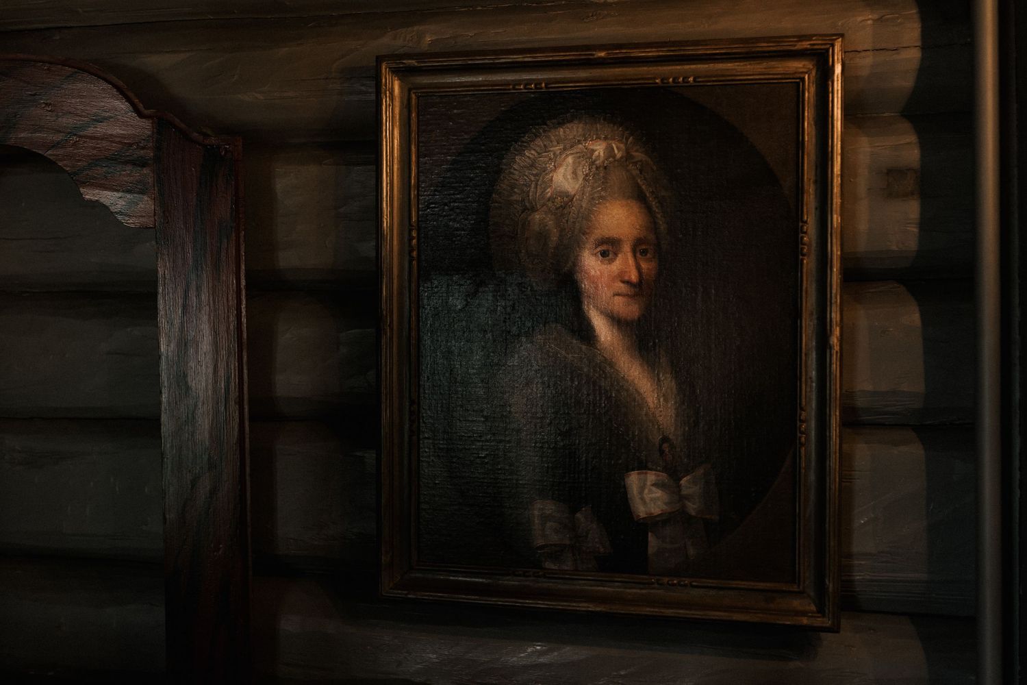 Antique-style portrait frames hang on a dark wooden wall in dramatic lighting.