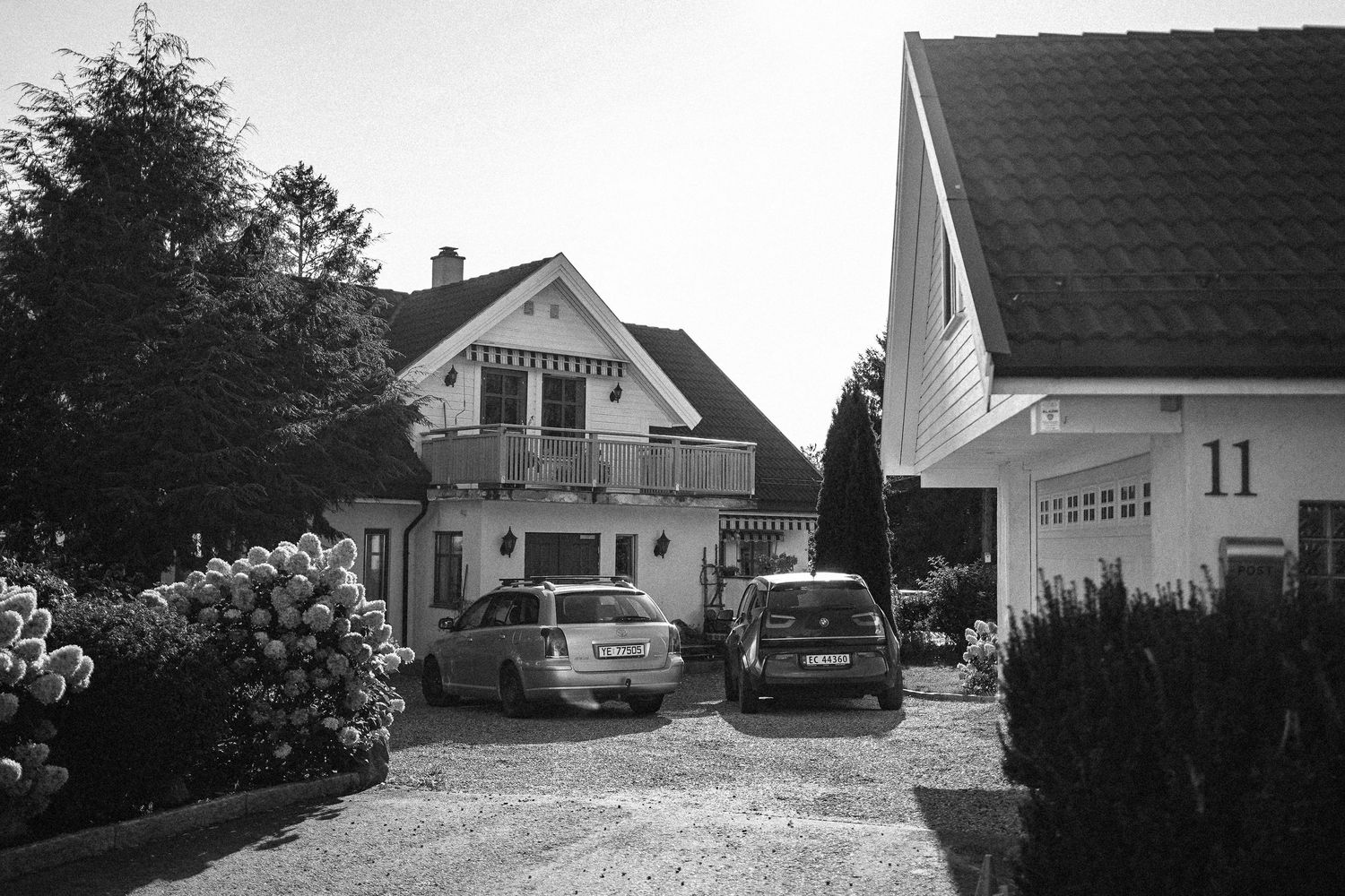 A series of modern suburban houses with white exteriors and dark roofs line up along a residential street.