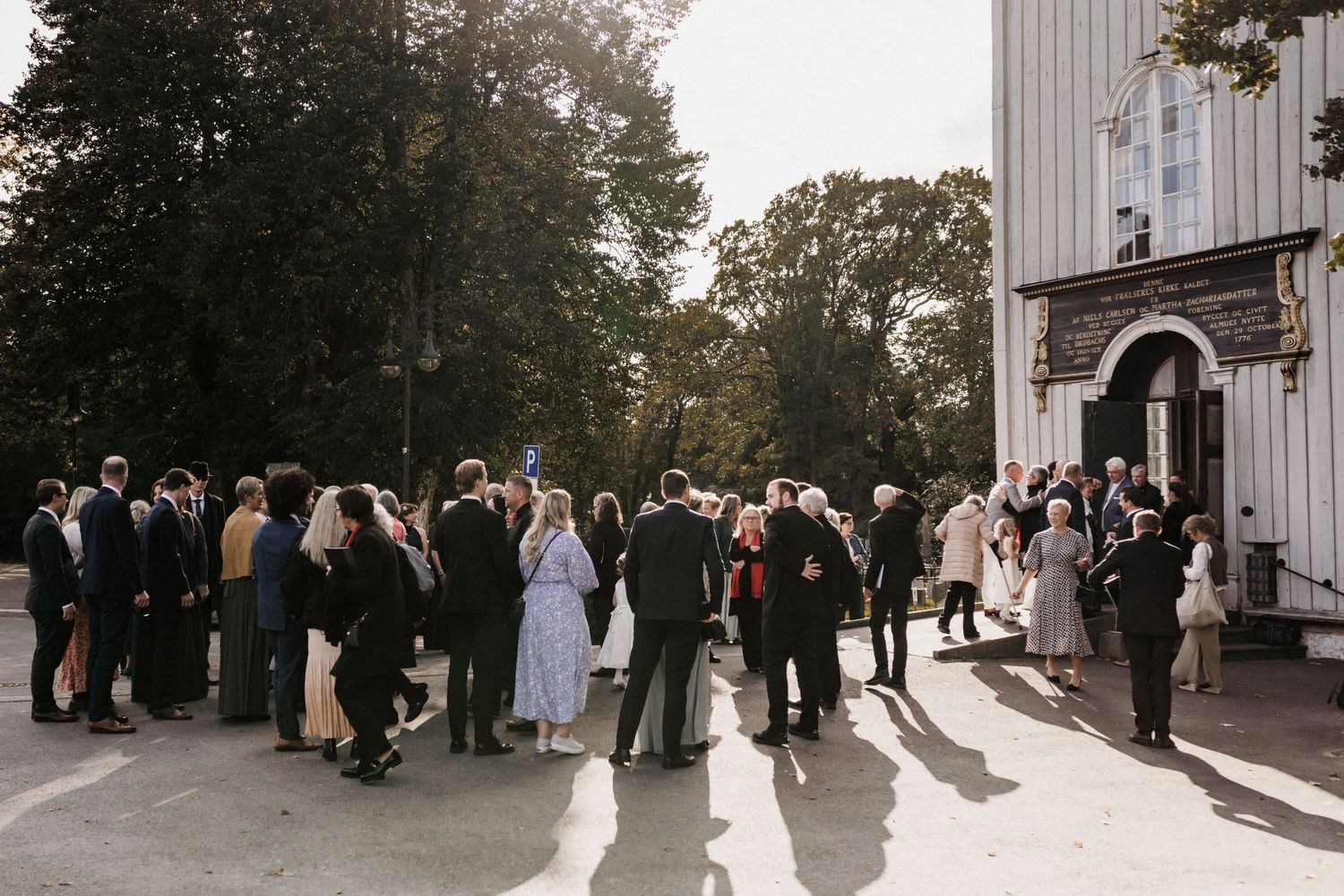 Wedding party and guests mingle outside a white church building.