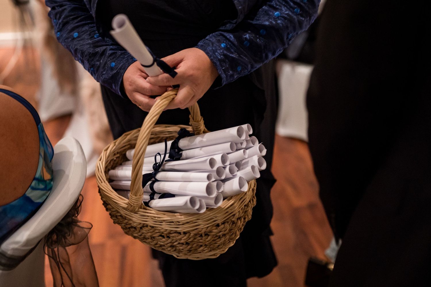 Close-up of hands holding a woven basket filled with rolled paper wedding programs.