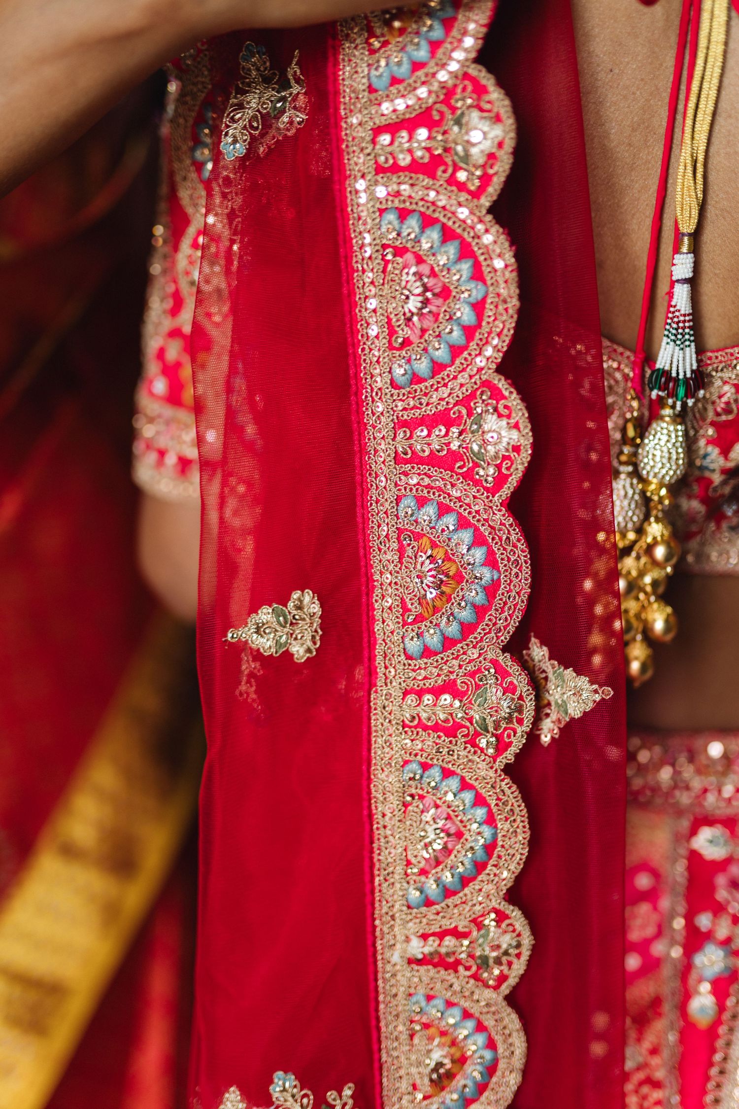 Intricate embroidery details on a red traditional Indian wedding sari with sparkling crystals and golden accents.