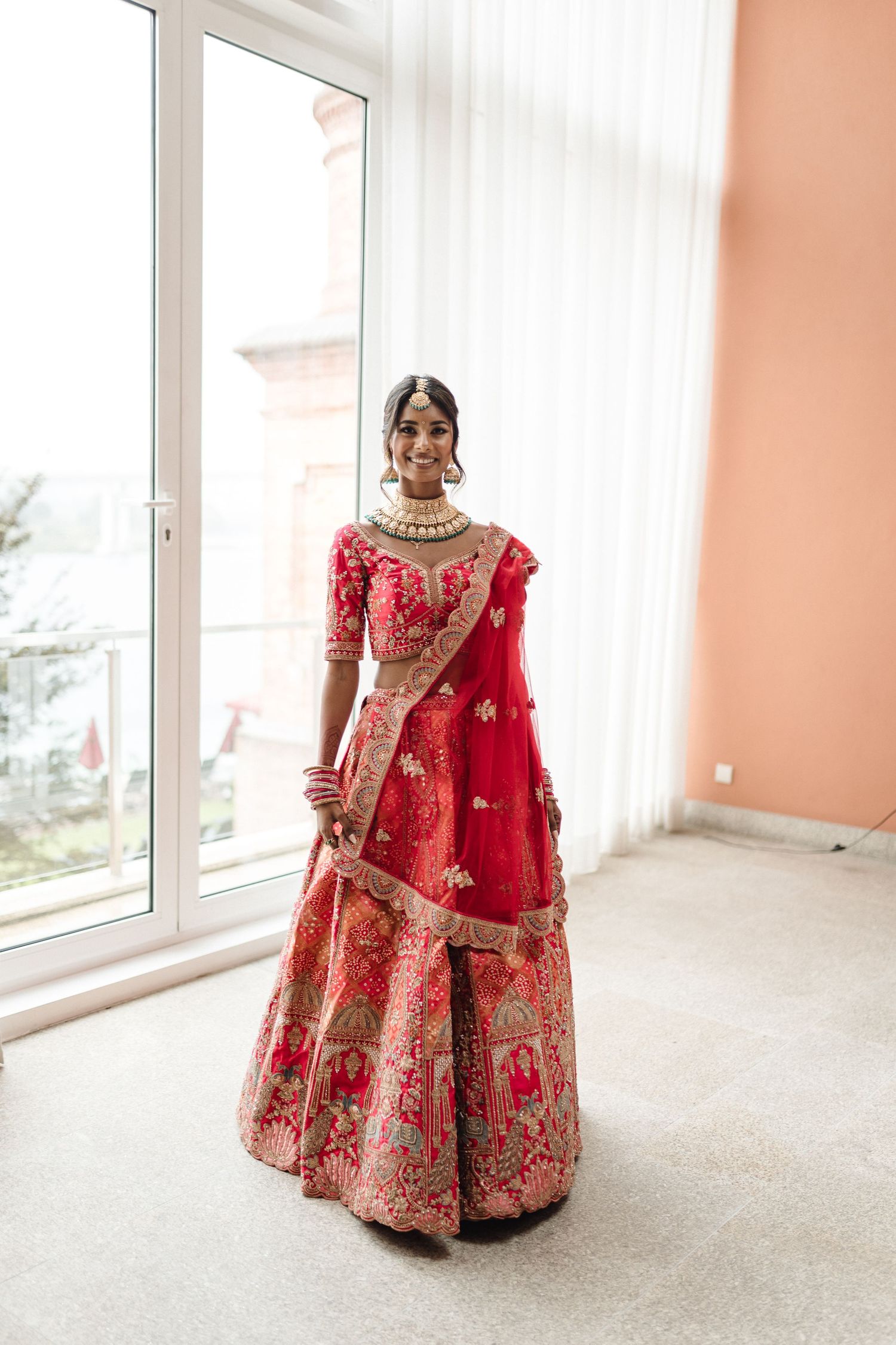 Stunning red and gold traditional bridal lehenga displayed in bright interior space.