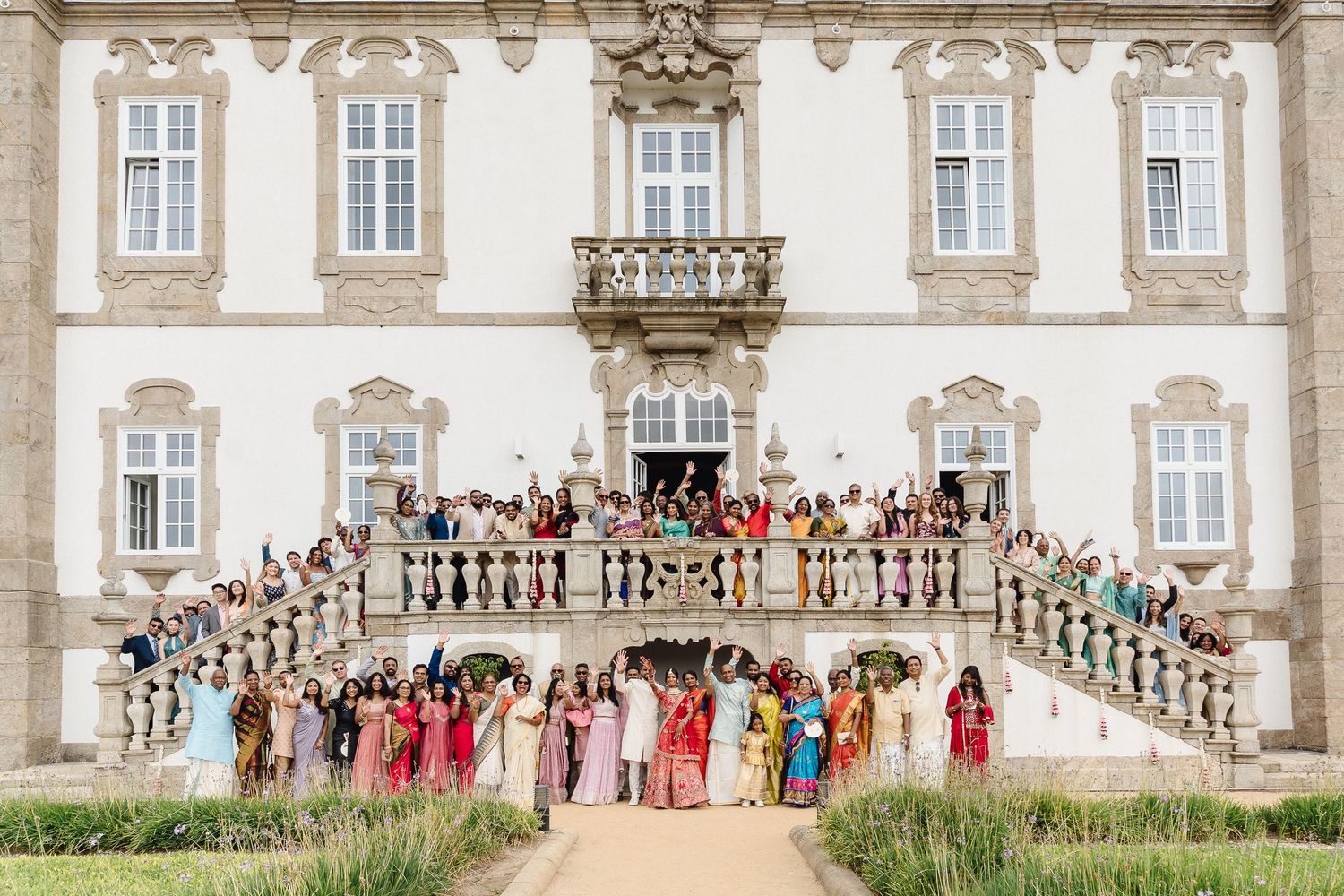 Panoramic view of wedding guests gathered on balcony of historic stone mansion.