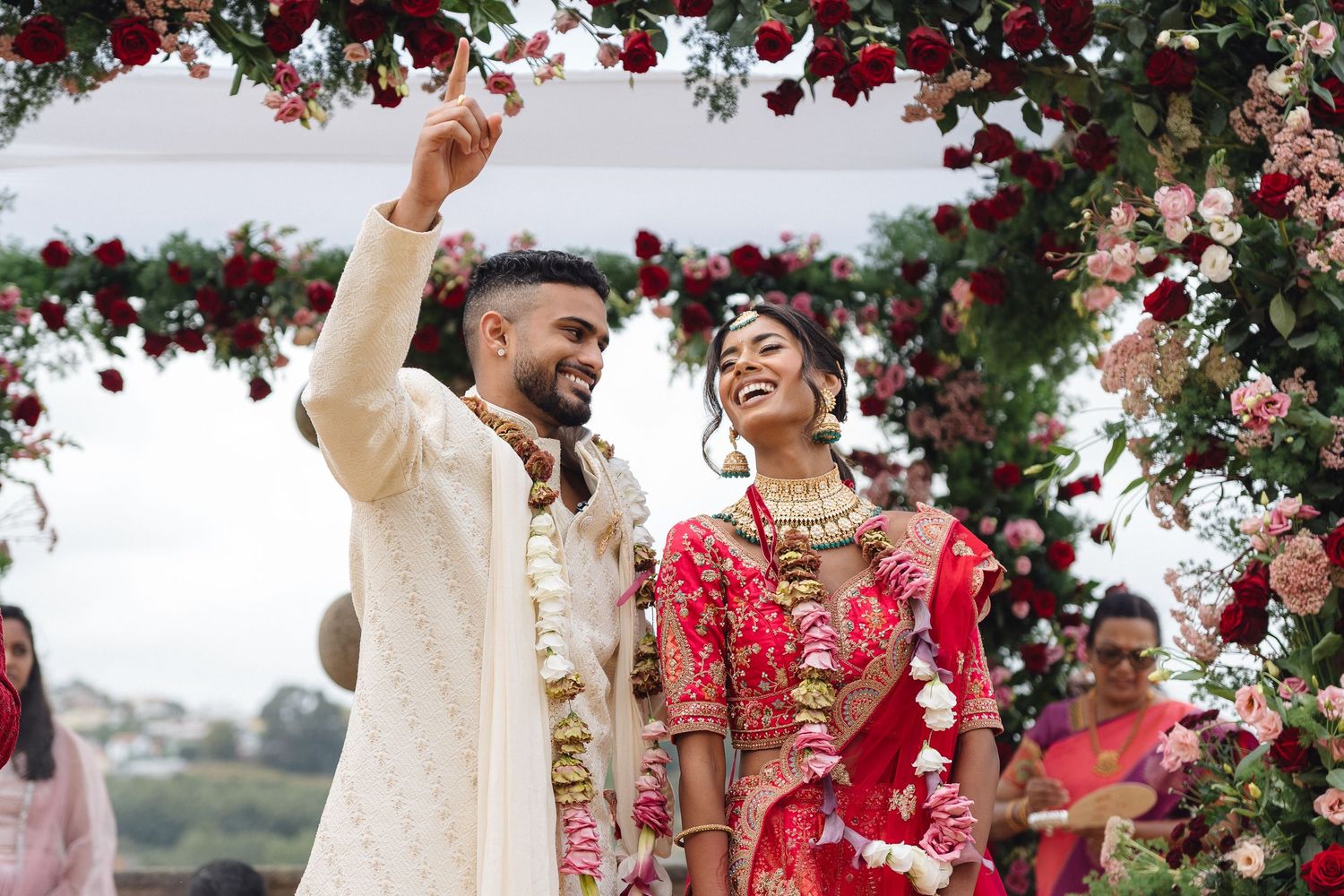 Wedding celebration under floral mandap with red roses and white draping.