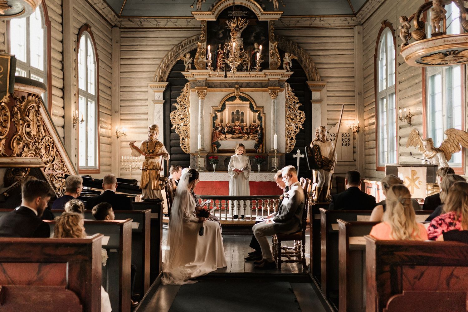 Traditional church wedding ceremony with wooden pews and ornate altar in natural lighting.