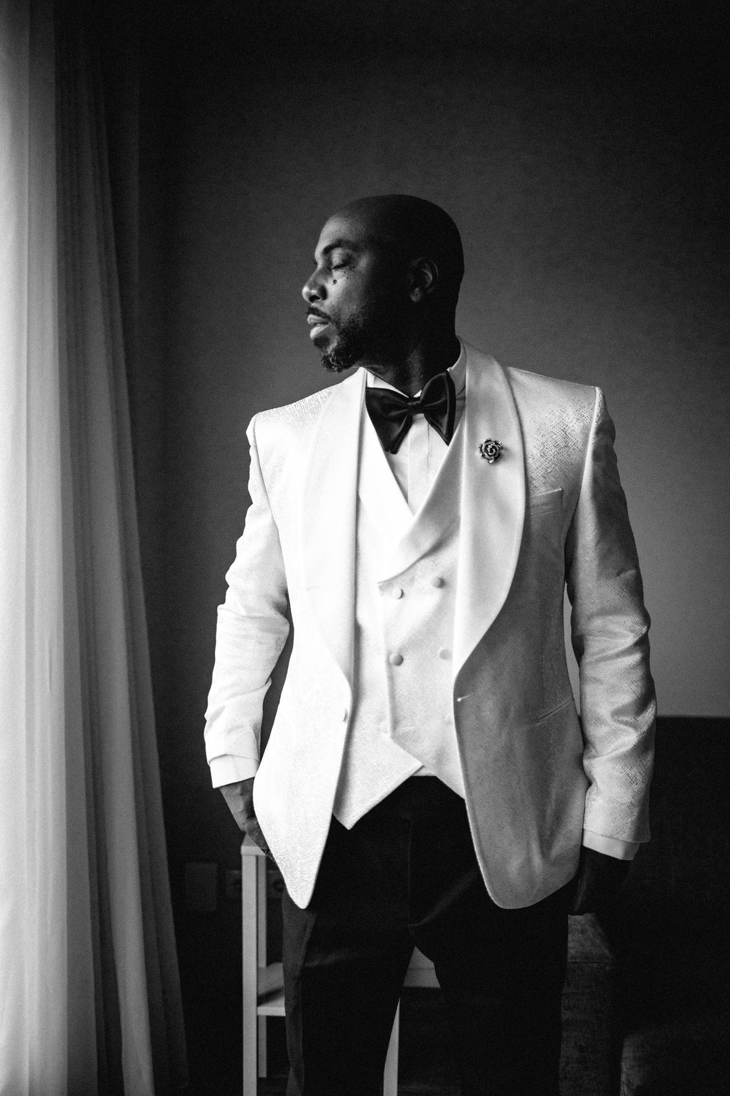 Stylish groom in white tuxedo jacket shown in dramatic black and white photography.