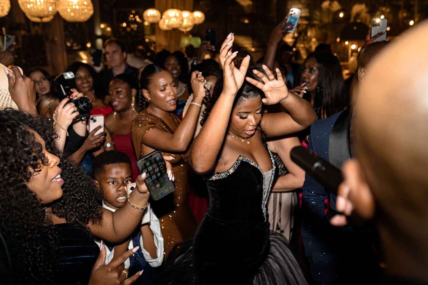 Guests dancing and celebrating at a lively wedding reception under glowing pendant lights.