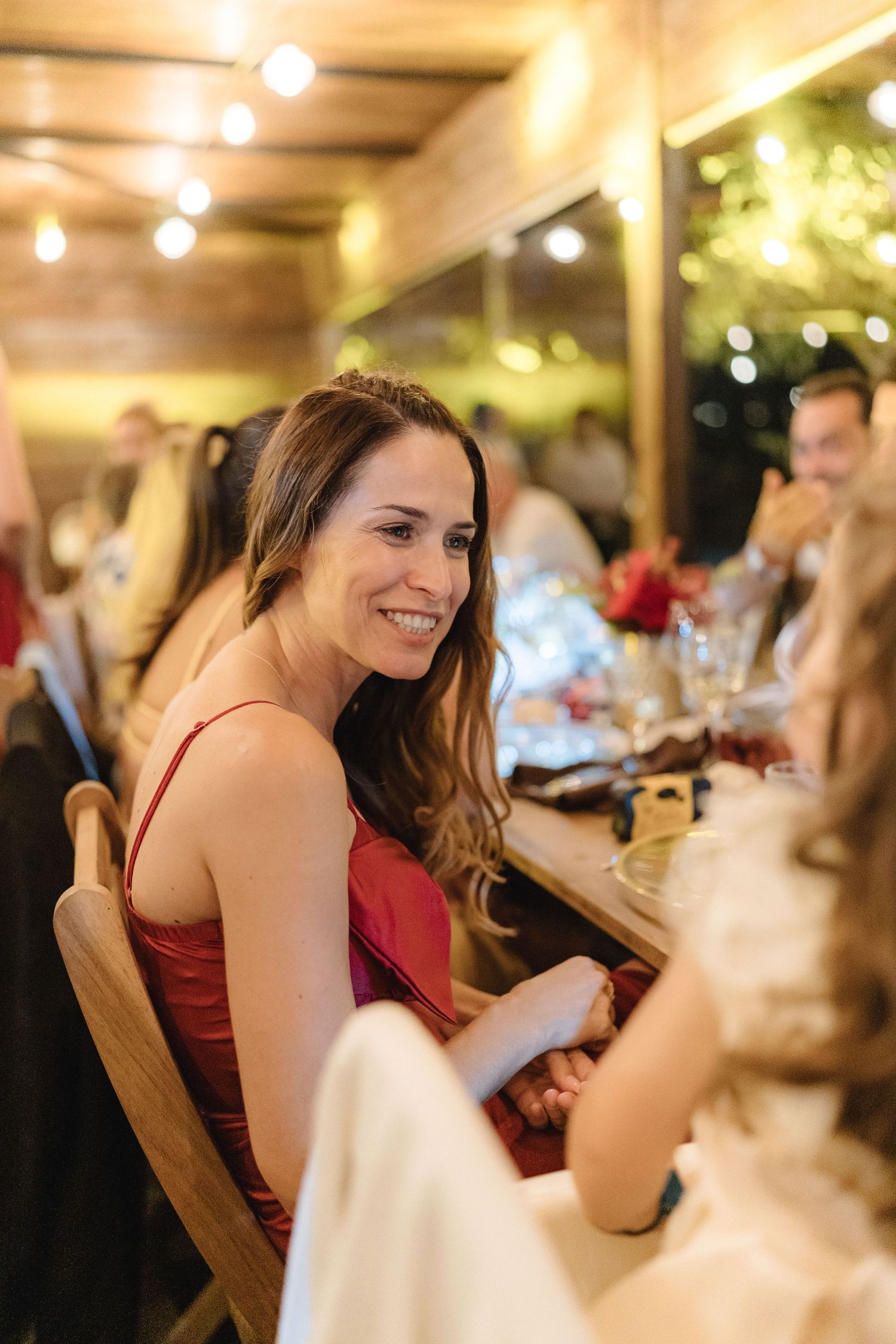 Guests in formal attire seated at a festive dinner table with ambient lighting and red decorations.