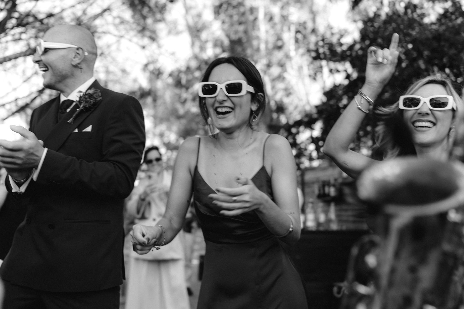 Wedding party members wearing sunglasses share a fun moment outdoors.
