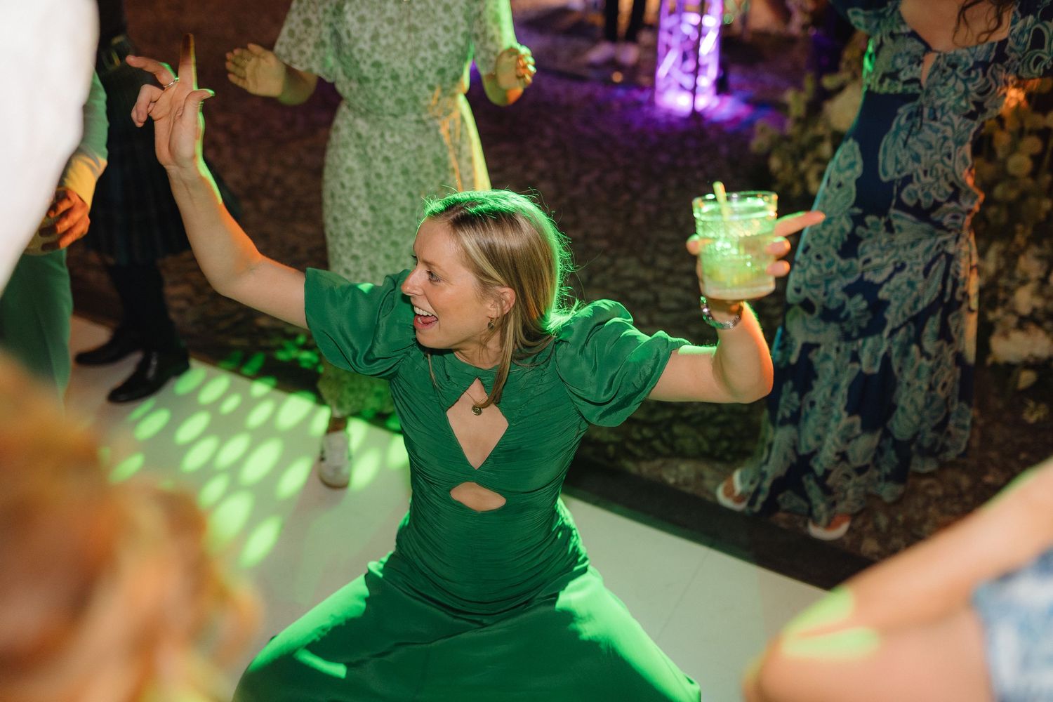 Dancers in green attire moving to the music under colorful party lights.