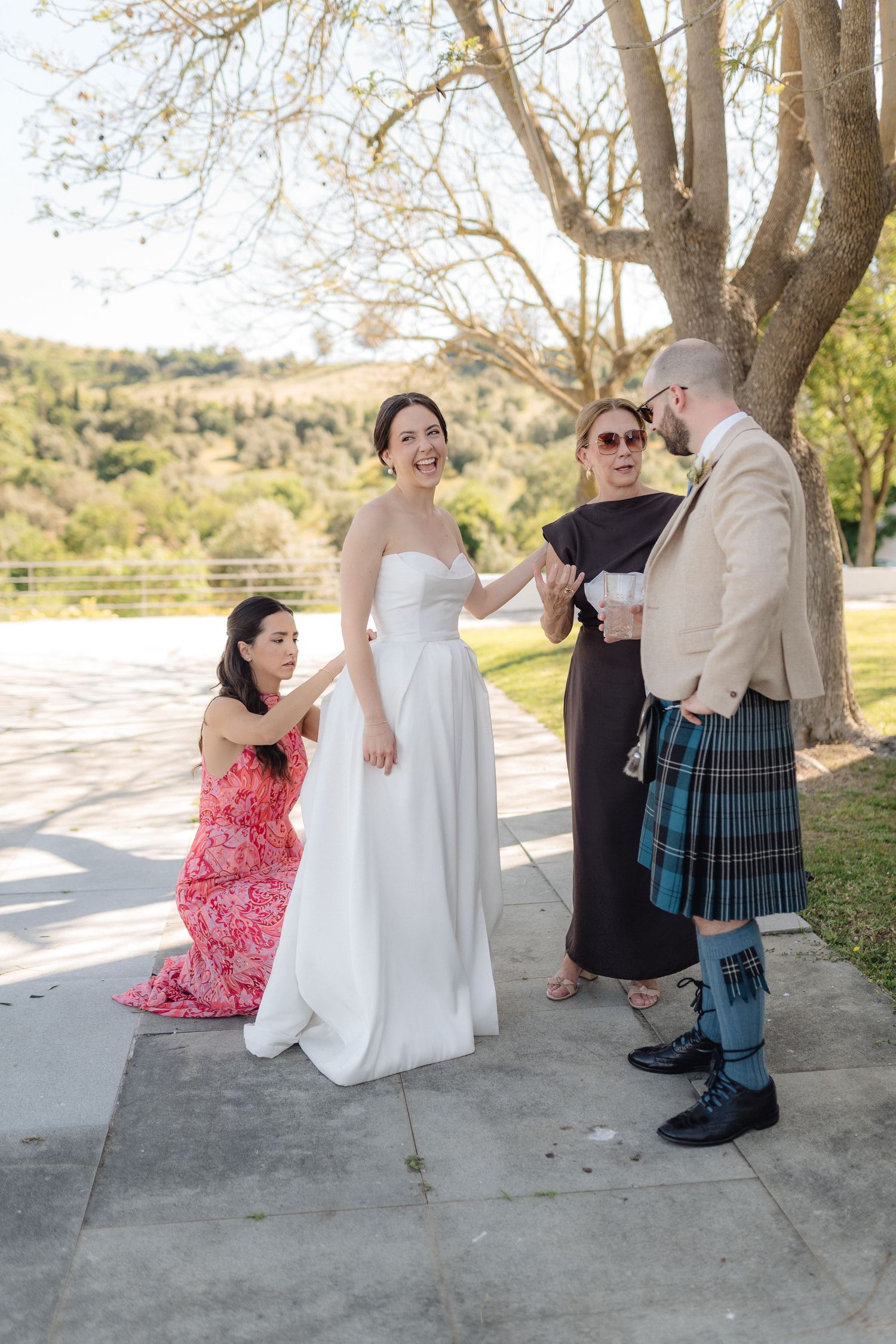 A wedding ceremony takes place outdoors with a person in a kilt and others in formal attire.