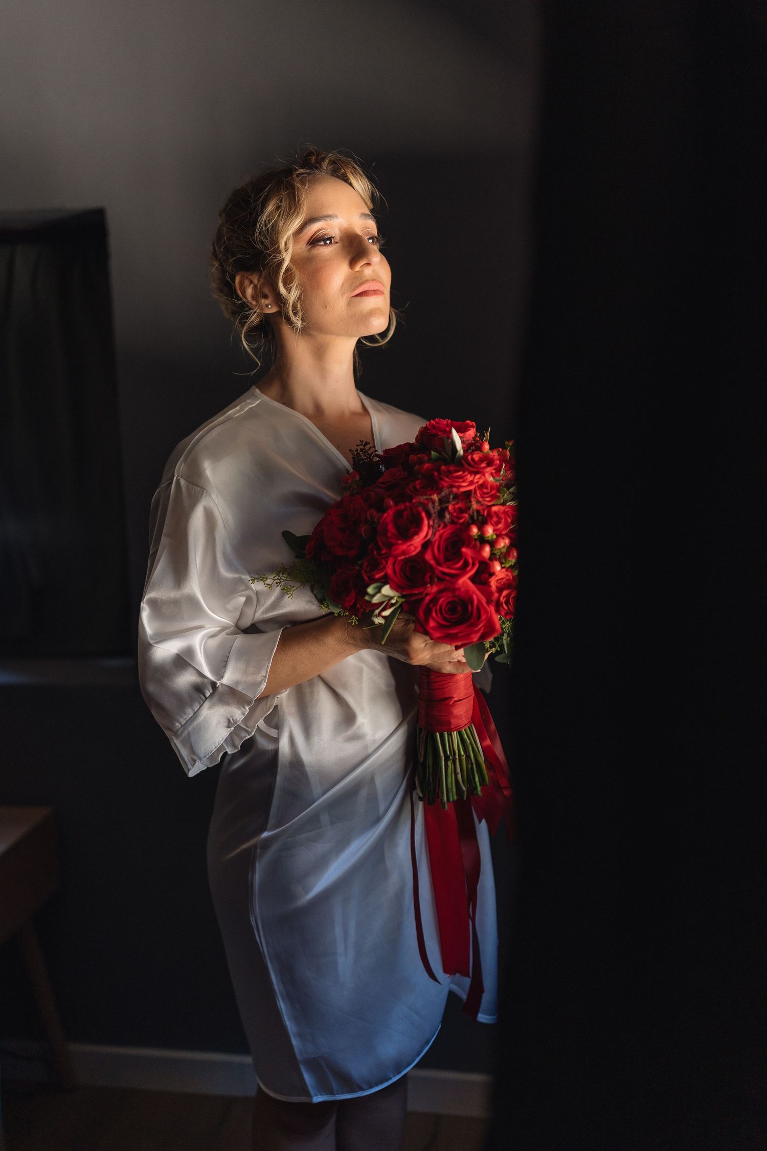 Artistic moody portrait with red rose bouquet in dramatic lighting.