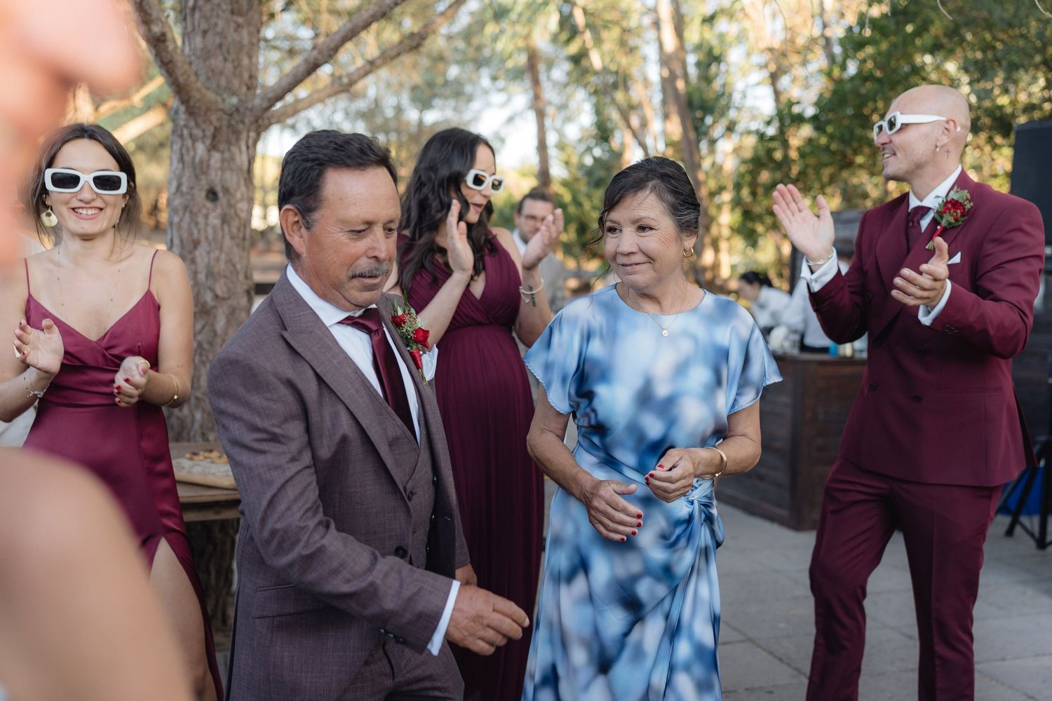 Wedding celebration with guests in burgundy and blue attire dancing outdoors.