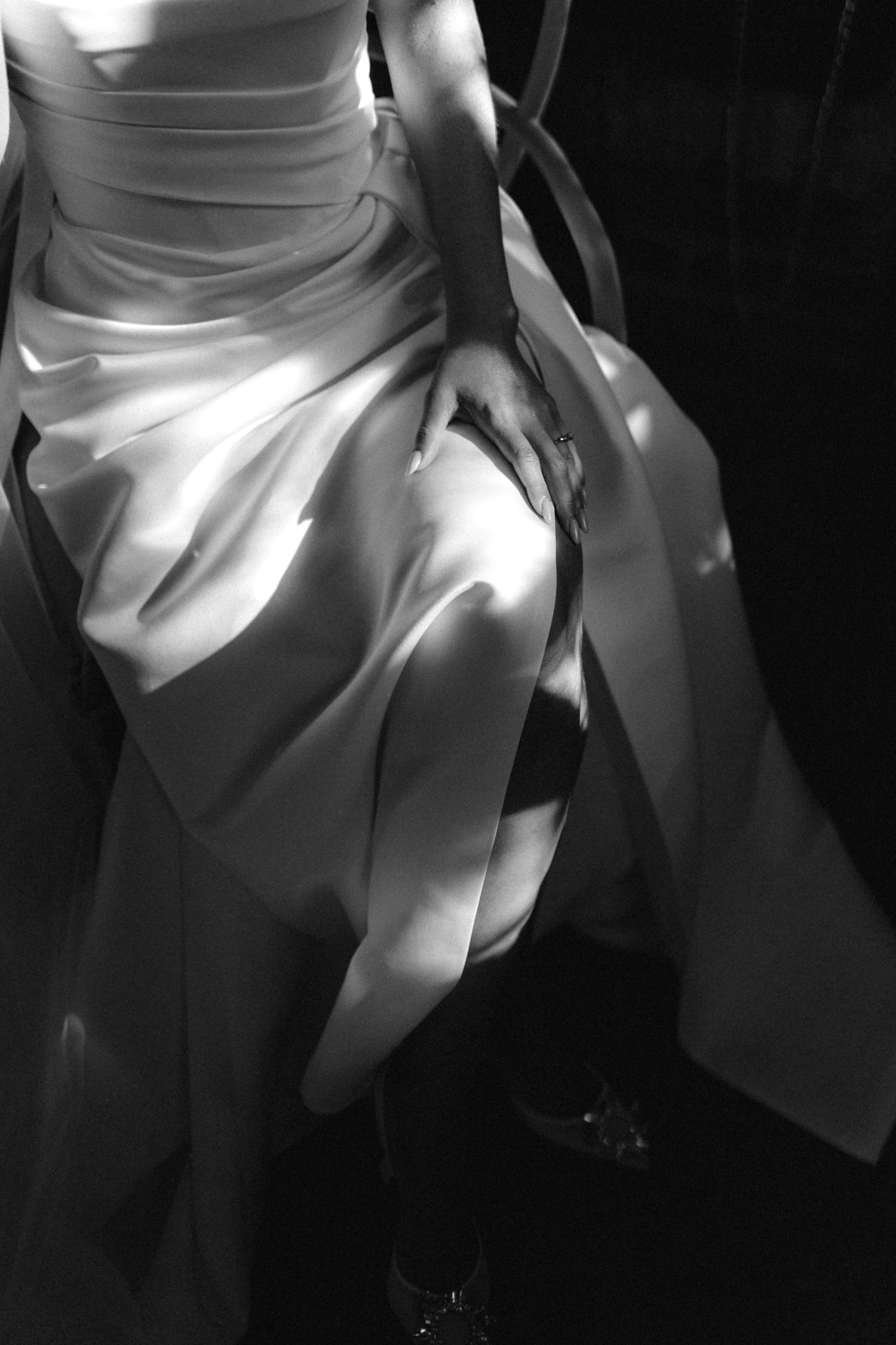 Black and white artistic photo of bride in voluminous satin wedding dress with dramatic light shadows.