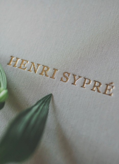 Close-up view of gold embossed text on a light gray textured surface with a blurred green leaf element in frame.