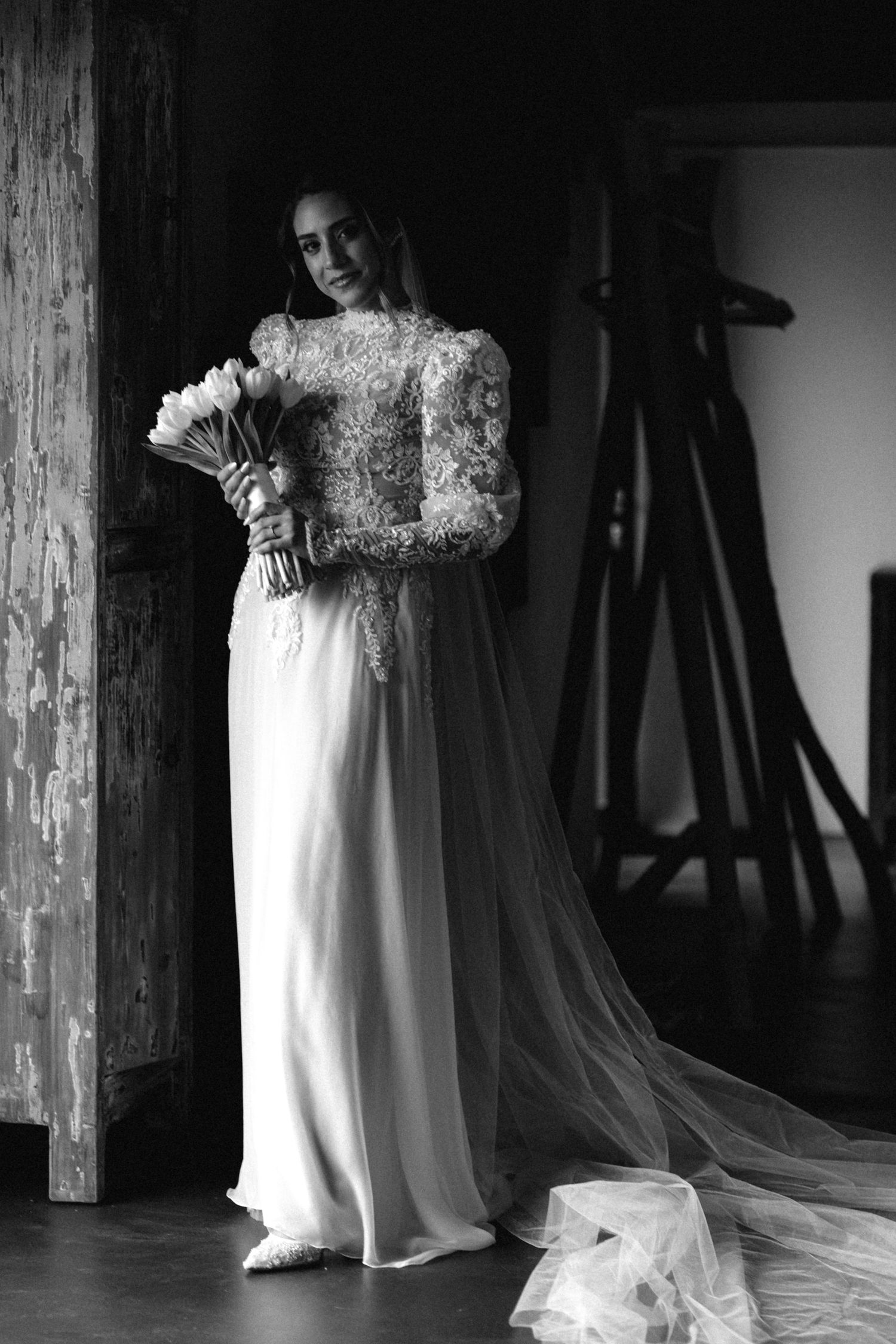 Wedding dress with intricate lace details and long train displayed in a dark rustic setting.