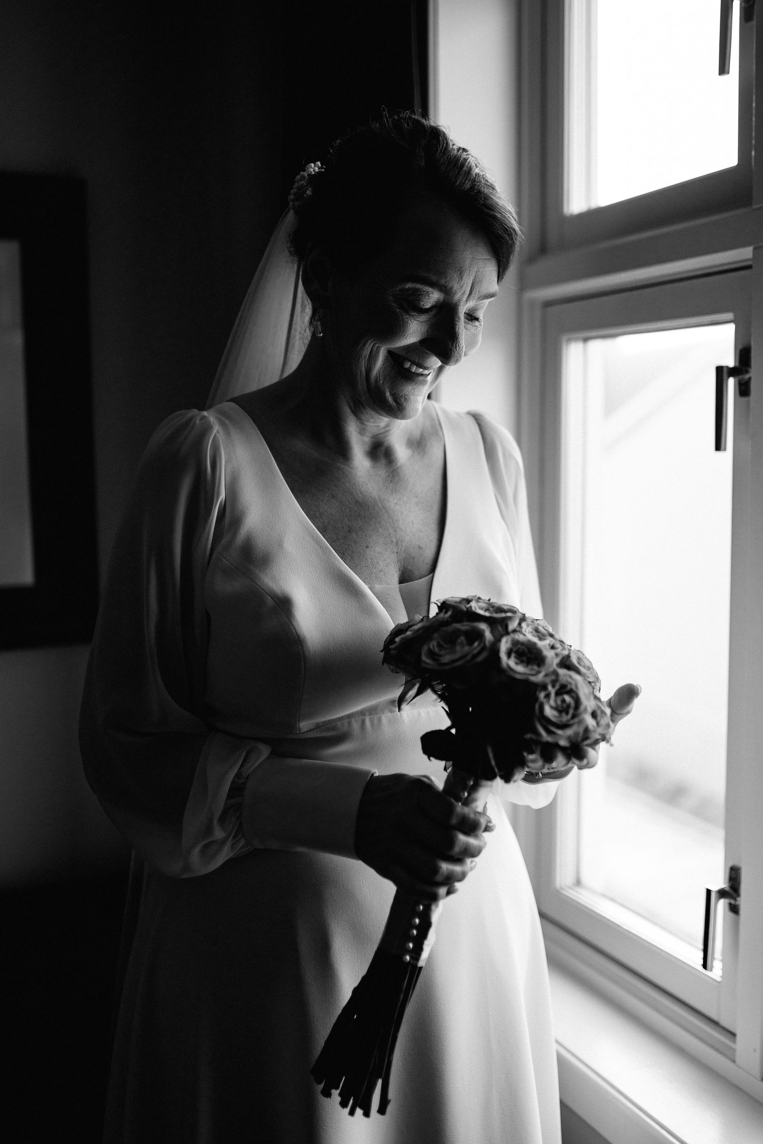 Elegant bridal preparation scene by a bright window with flowing white dress details.