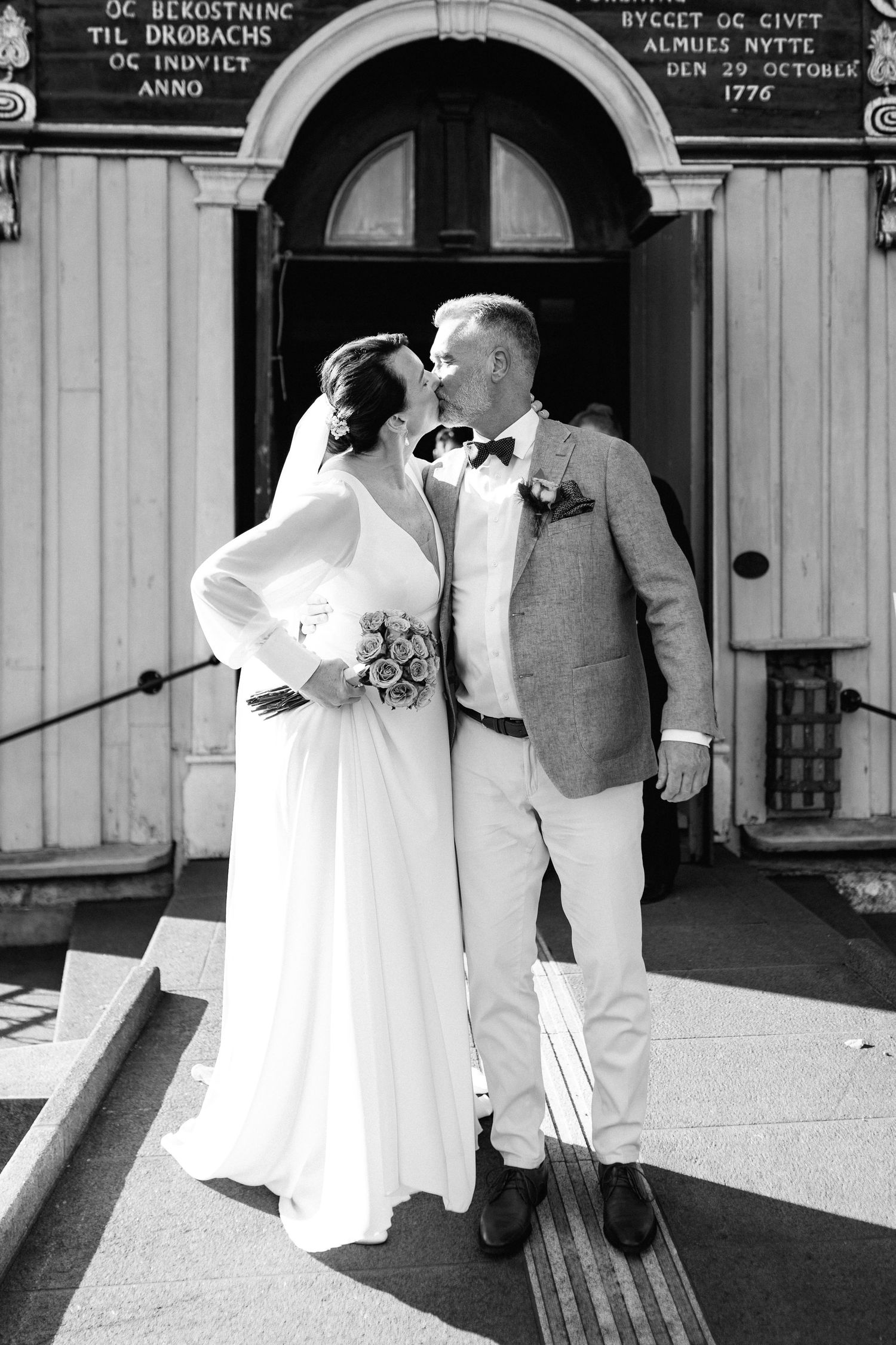 A couple shares a romantic moment outside a historic white church building.